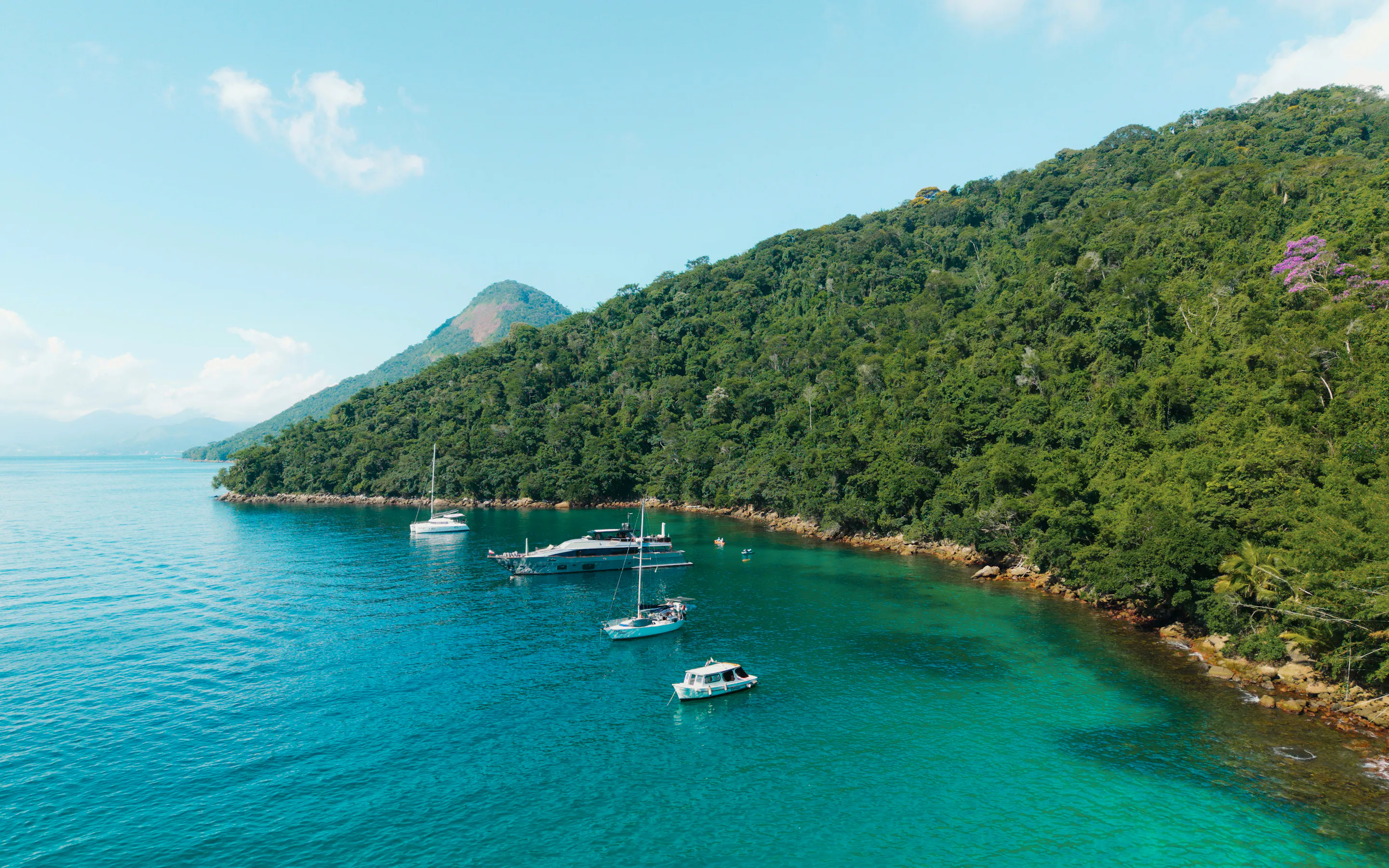 Sailboats anchor in calm turquoise water beside a densely forested green island at Ilha Grande.