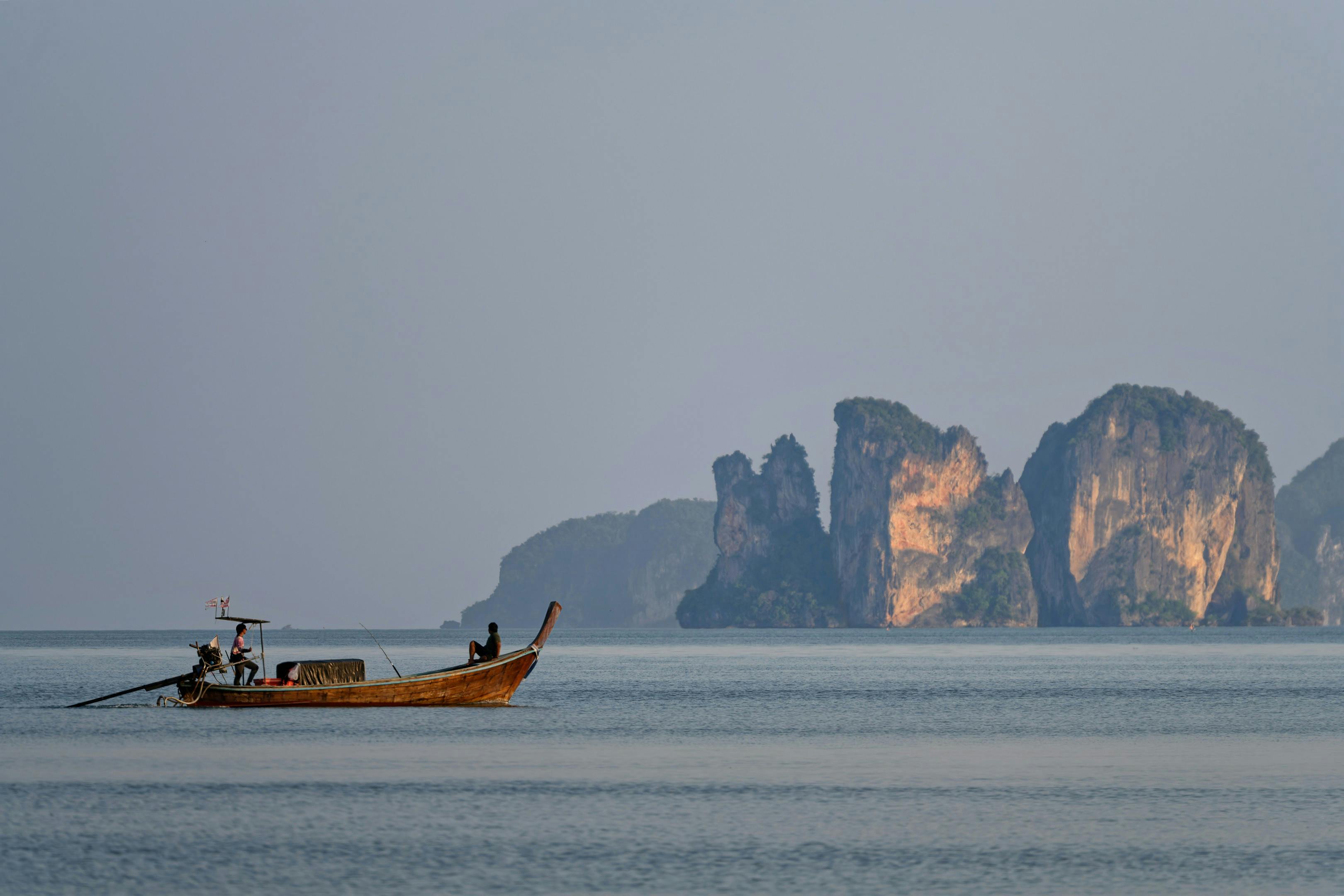 A longtail boat anchors in a cove flanked by sheer limestone cliffs rising from turquoise water.