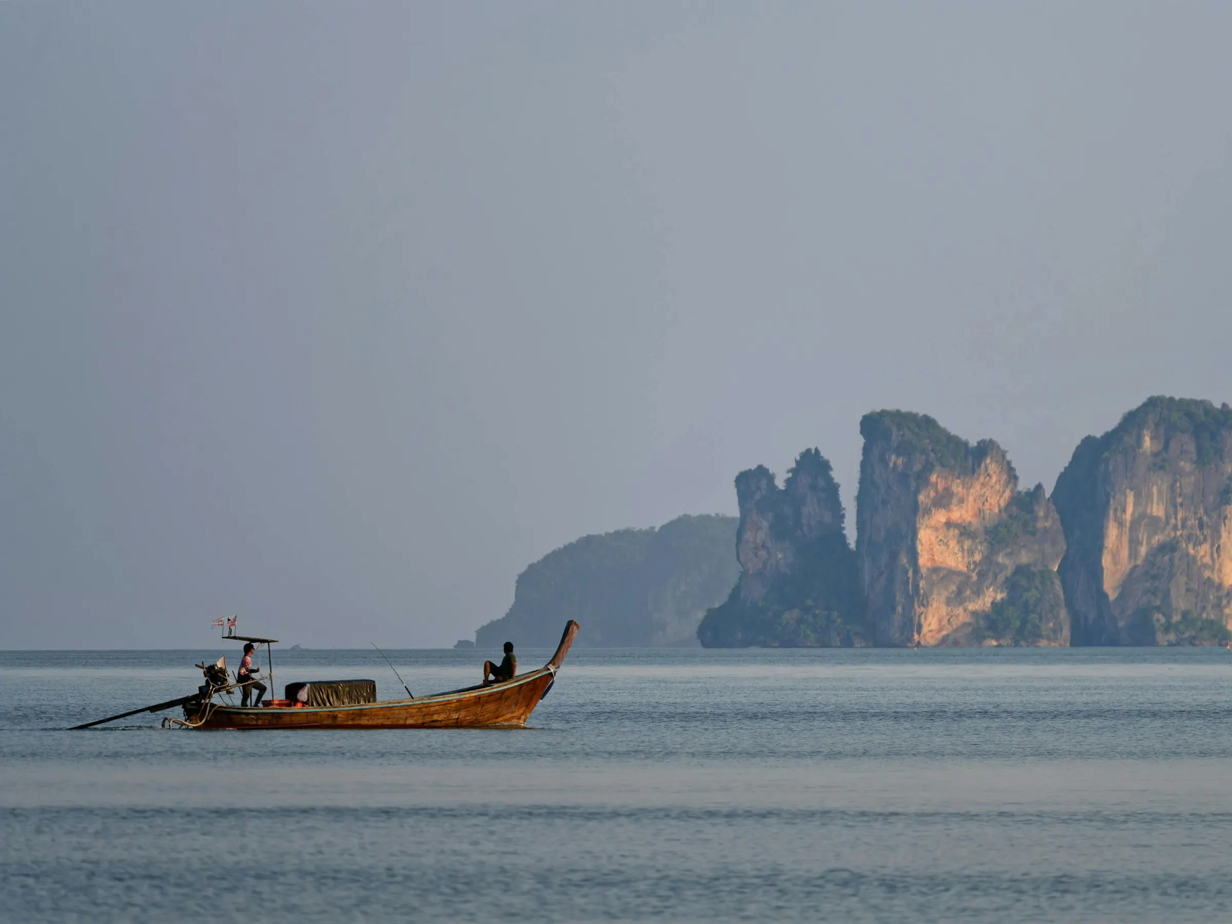 A longtail boat anchors in a cove flanked by sheer limestone cliffs rising from turquoise water.