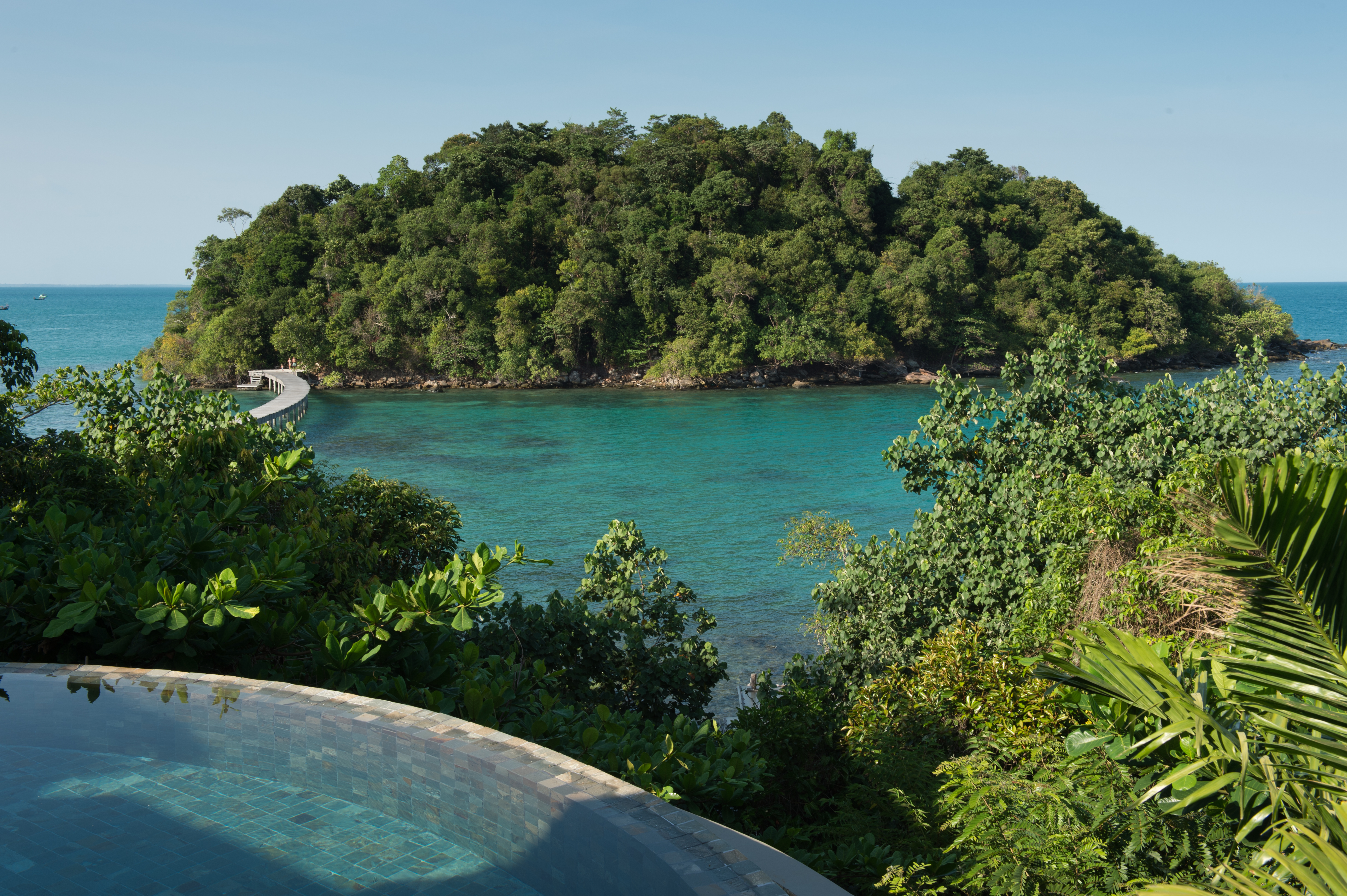 An overwater villa with a thatched roof and wooden deck extends above turquoise sea at Song Saa.