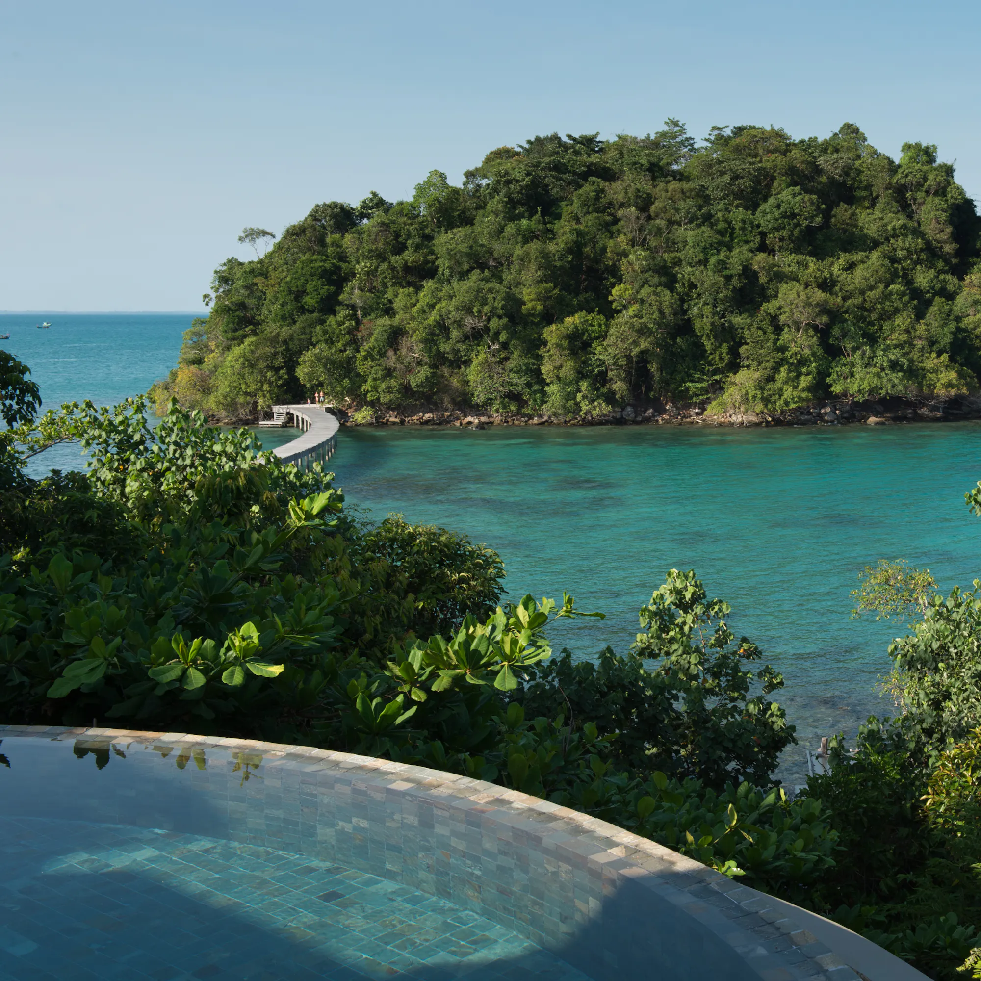 An overwater villa with a thatched roof and wooden deck extends above turquoise sea at Song Saa.