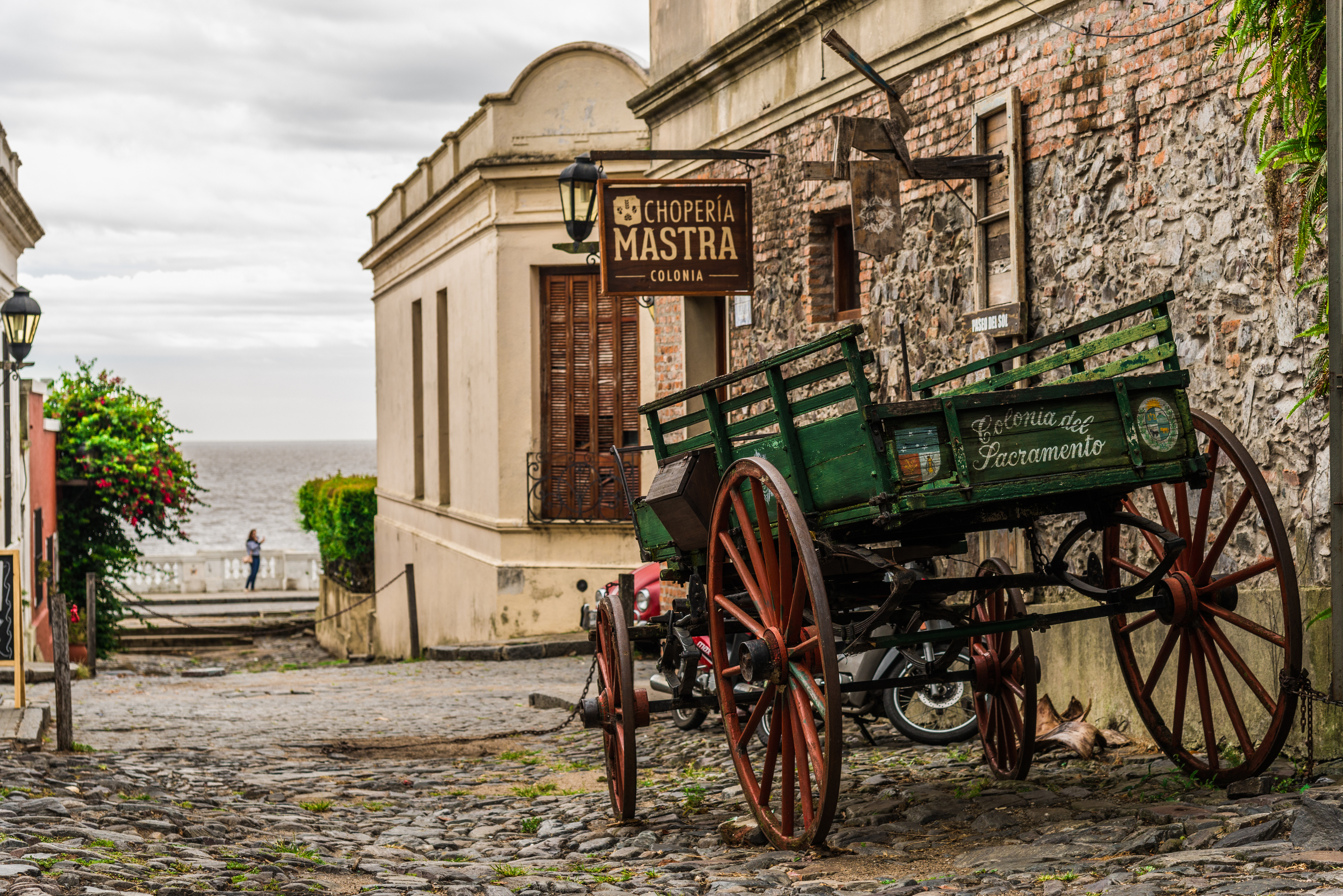 An old wooden cart sits on a stone-paved plaza in front of a colonial building in Uruguay.