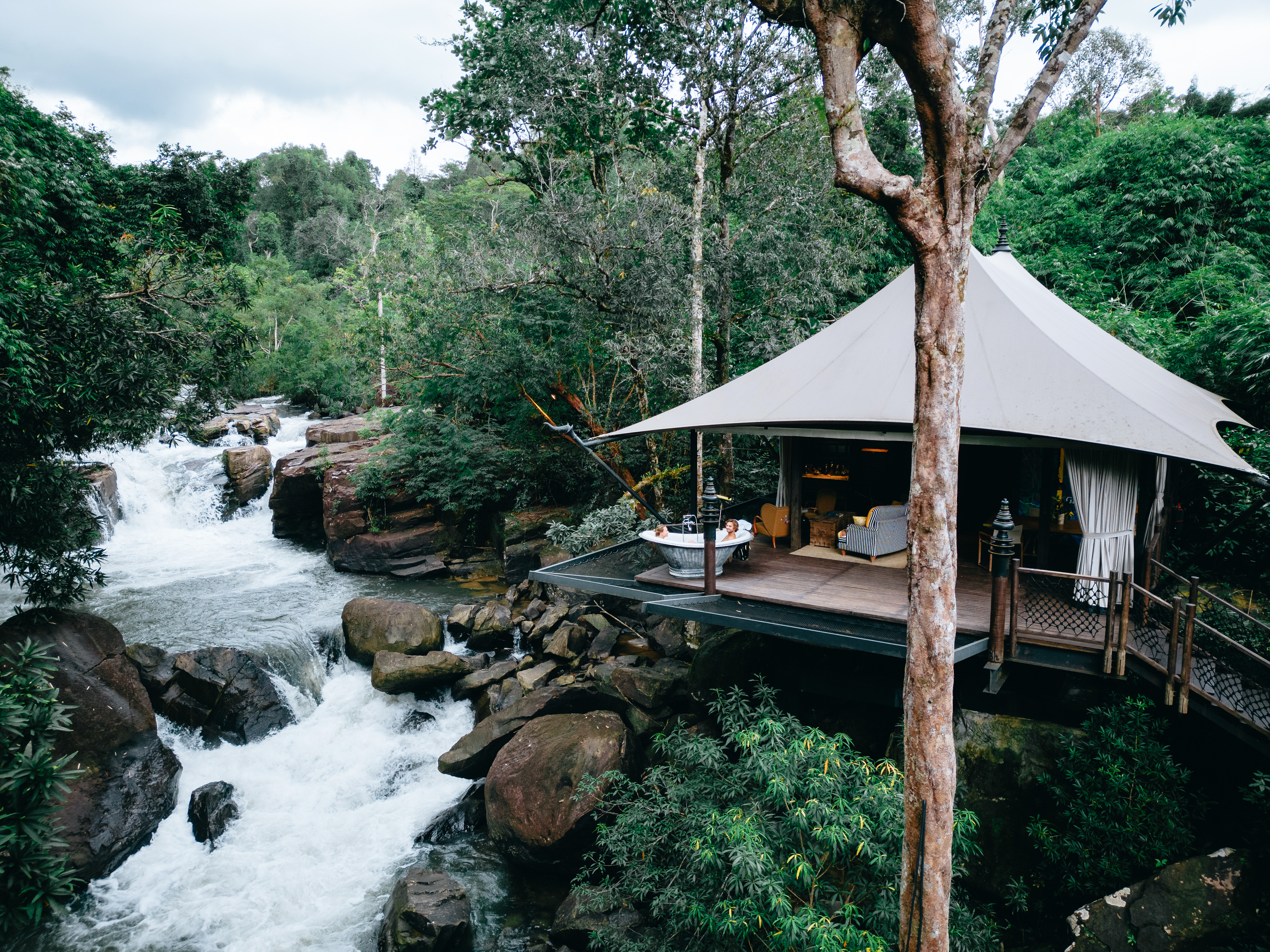A raised tented lodge terrace overlooks a rushing jungle waterfall in Cambodia's Cardamom Mountains.
