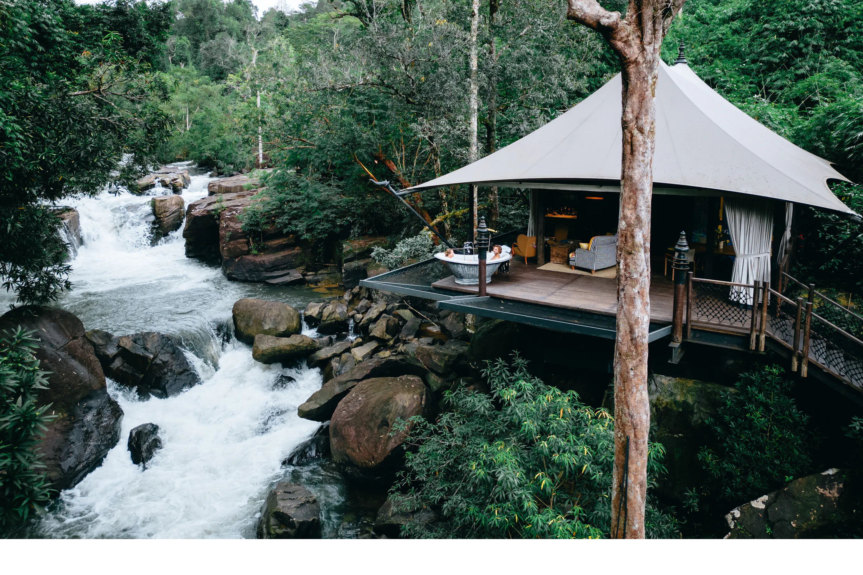 A raised tented lodge terrace overlooks a rushing jungle waterfall in Cambodia's Cardamom Mountains.