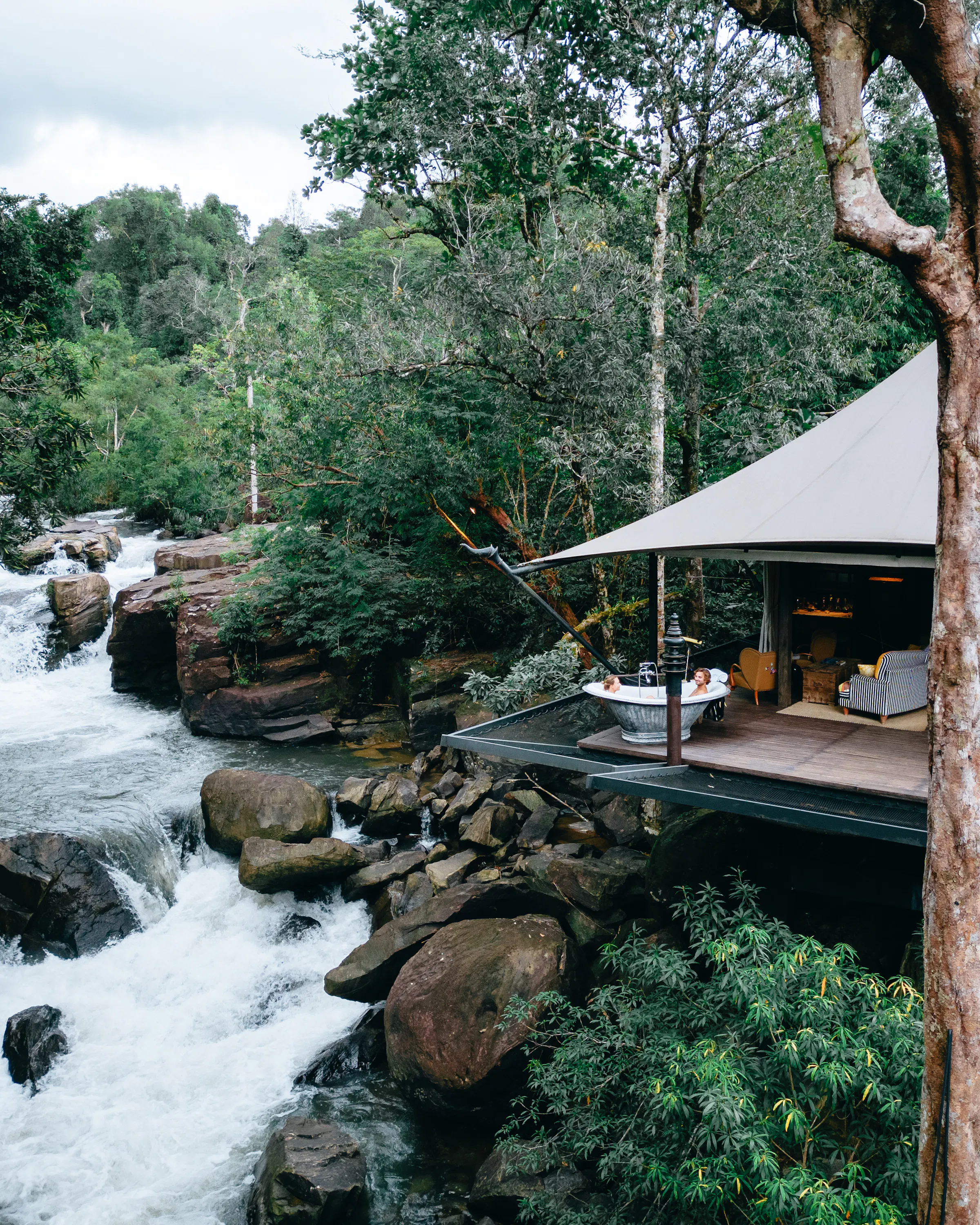 A raised tented lodge terrace overlooks a rushing jungle waterfall in Cambodia's Cardamom Mountains.