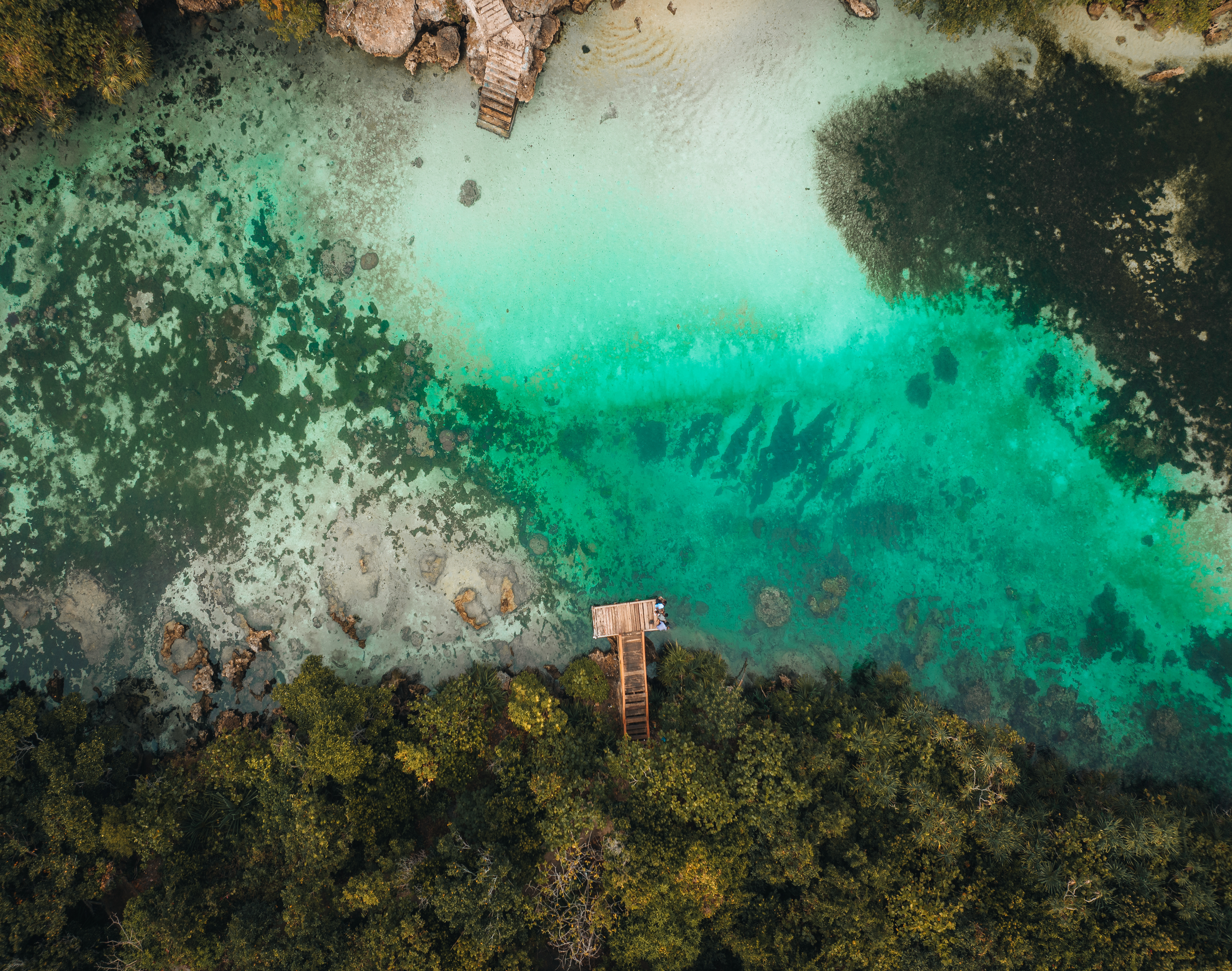 Aerial view of a vivid turquoise lagoon bordered by forested cliffs and pale sandy beaches in Sumba.