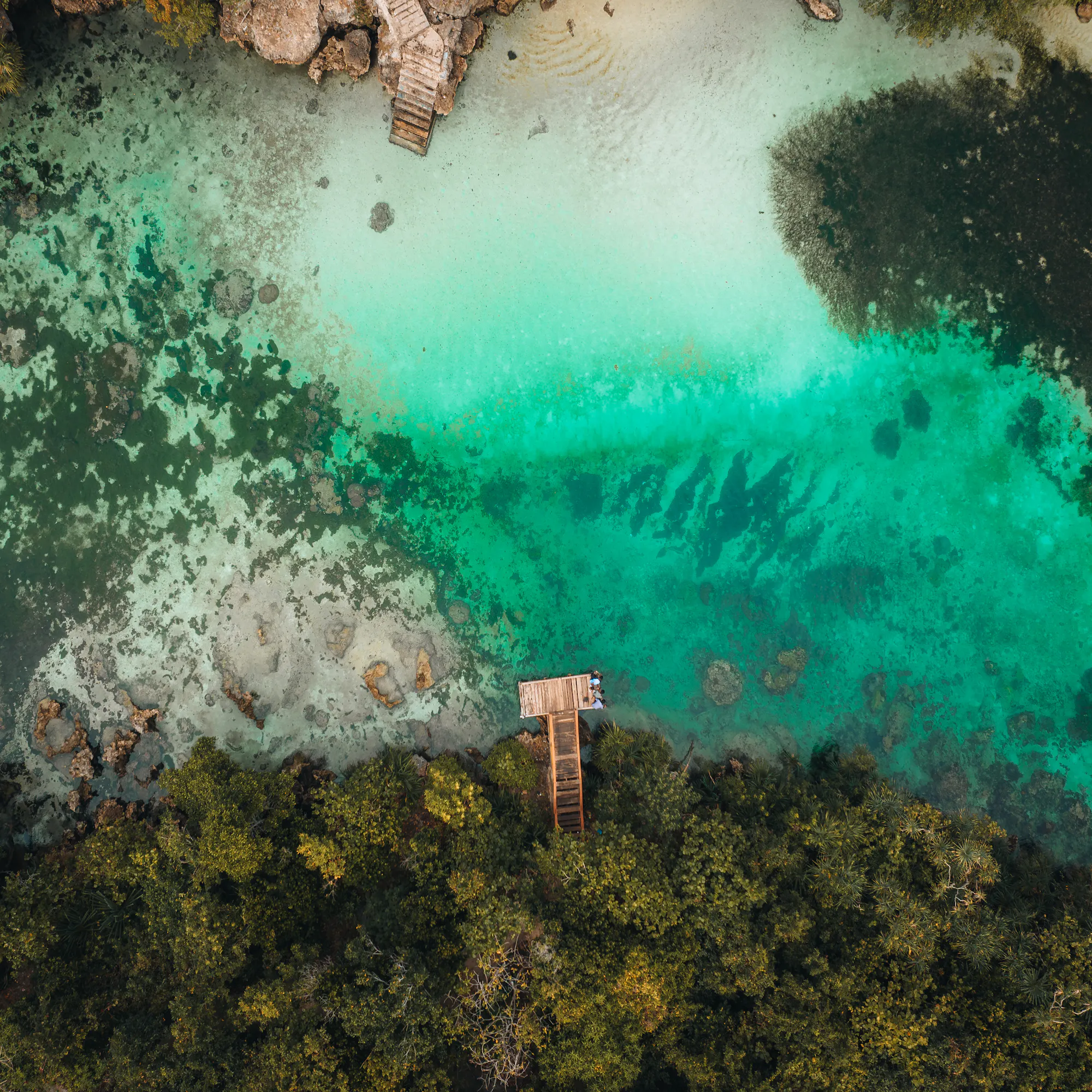 Aerial view of a vivid turquoise lagoon bordered by forested cliffs and pale sandy beaches in Sumba.