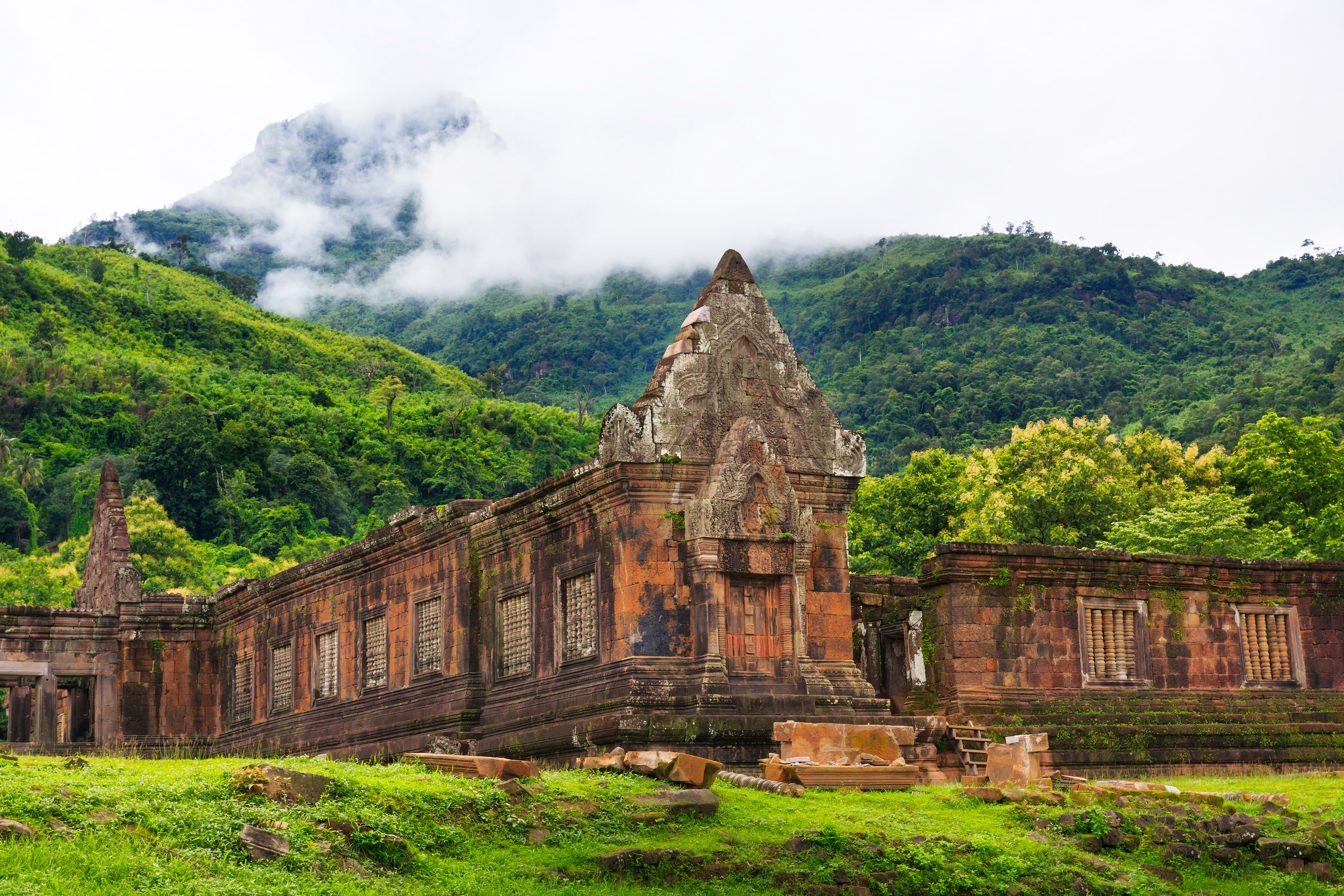 Ancient sandstone temple ruins rise from a green jungle hillside at Wat Phou in Laos.