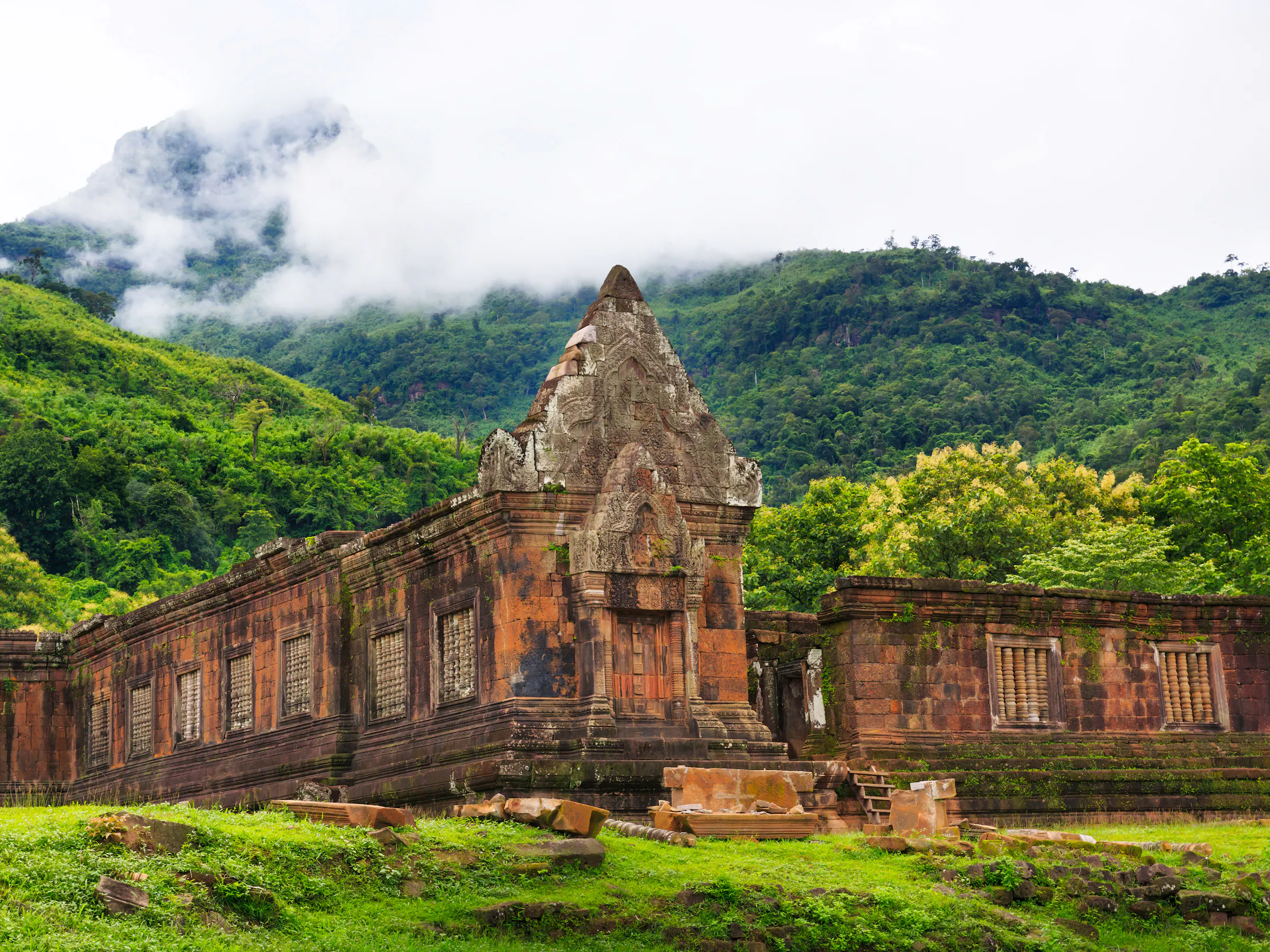 Ancient sandstone temple ruins rise from a green jungle hillside at Wat Phou in Laos.