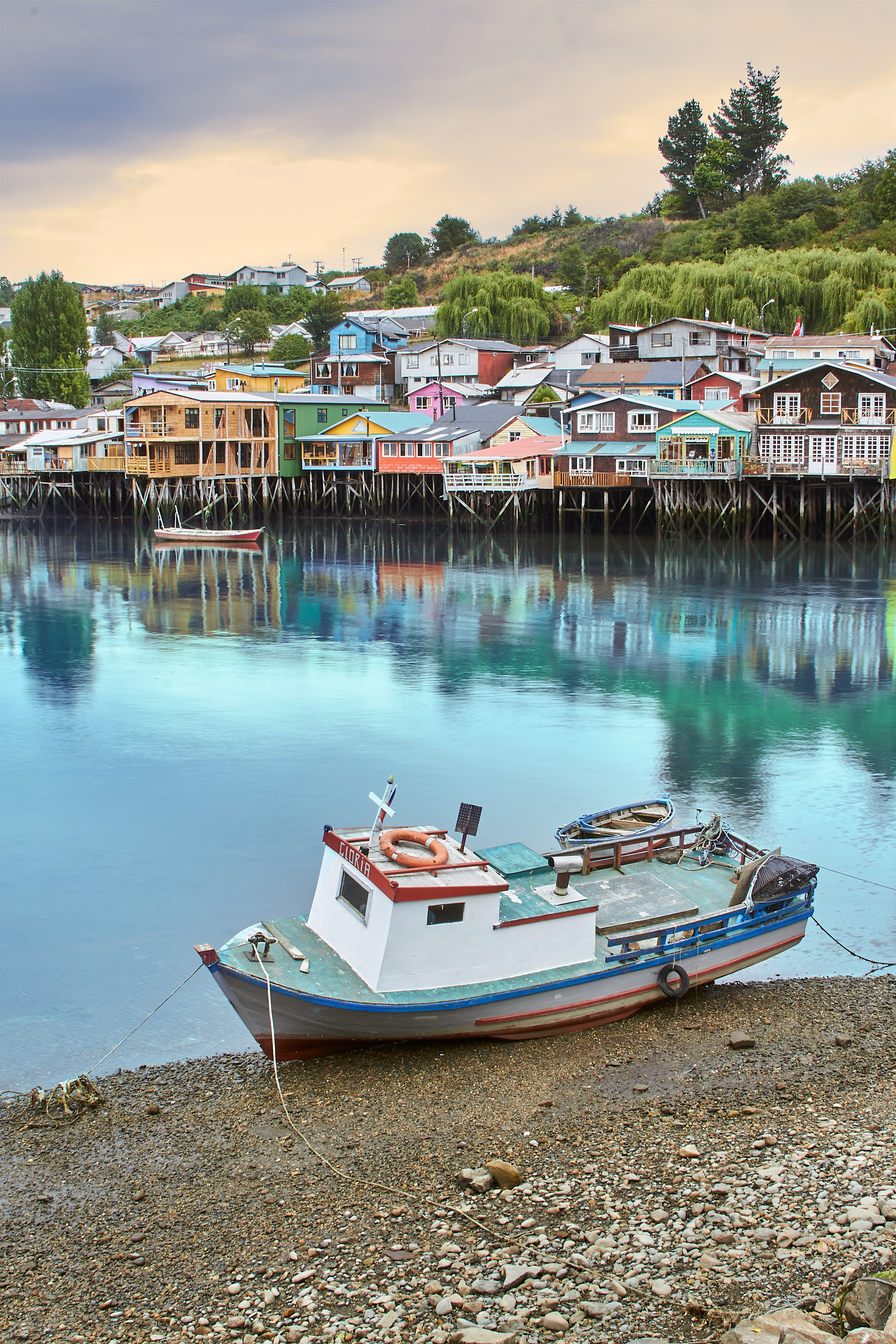 Colorful stilted wooden houses line a waterfront with small boats moored below in southern Chile.