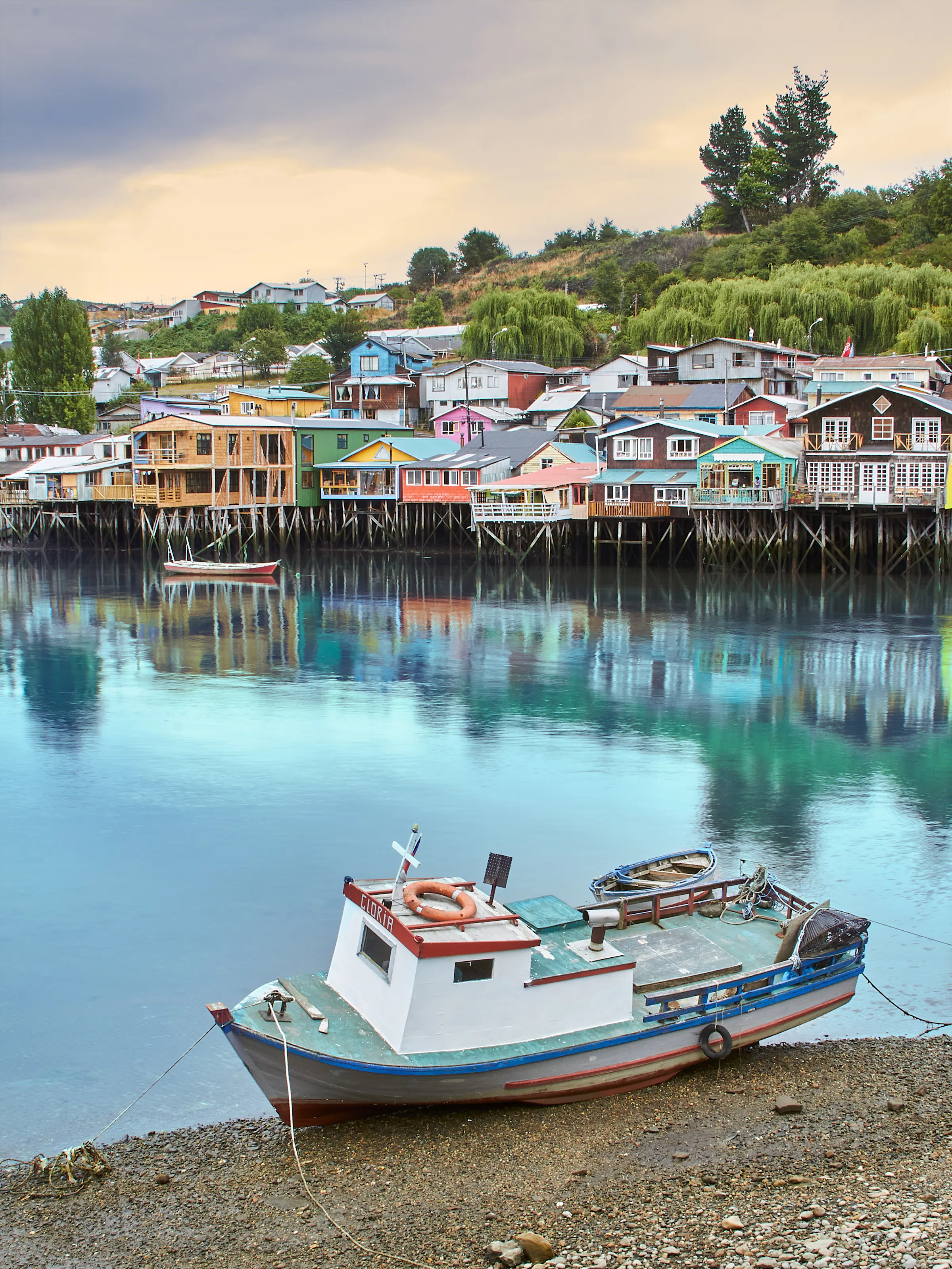 Colorful stilted wooden houses line a waterfront with small boats moored below in southern Chile.