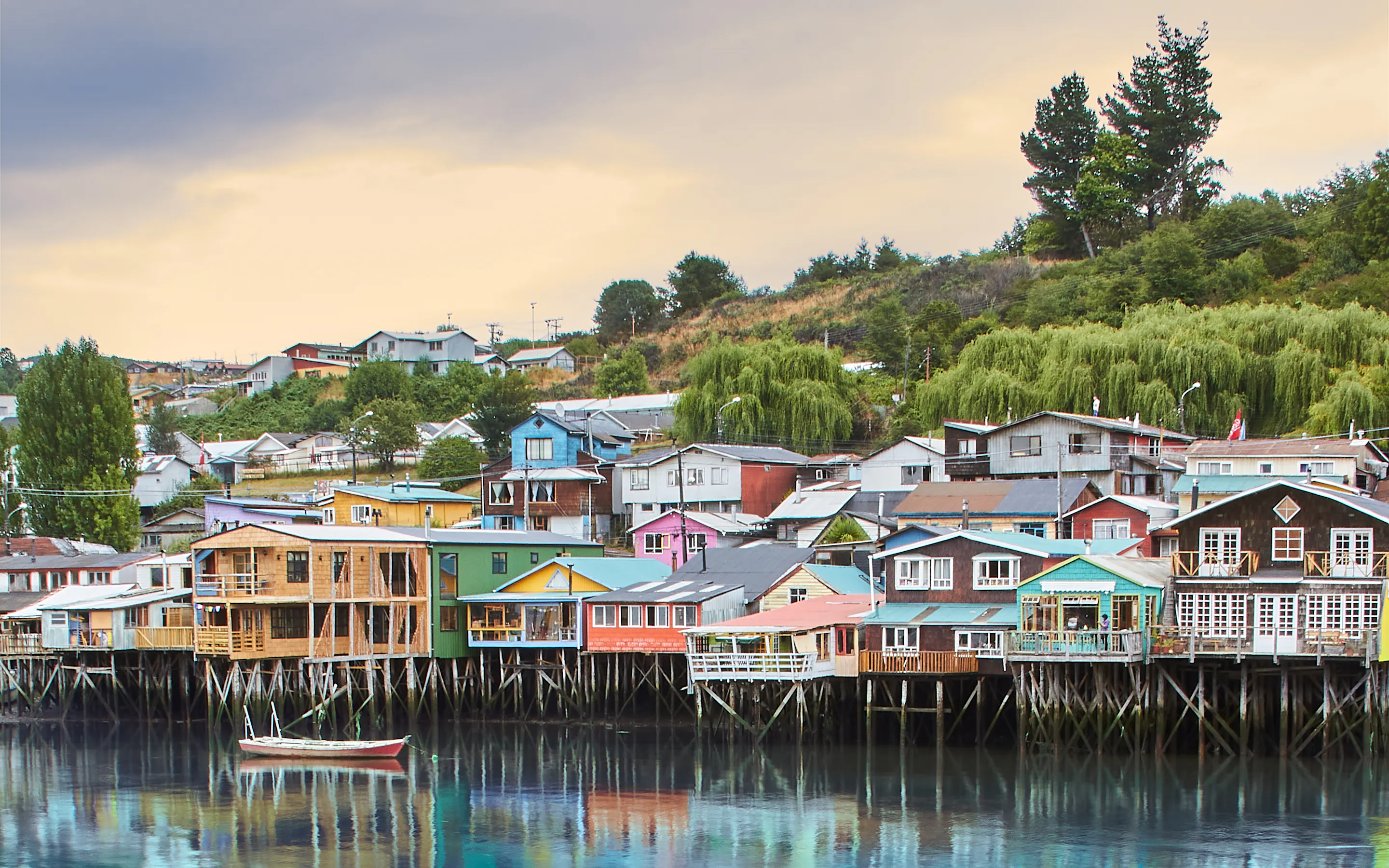 Colorful stilted wooden houses line a waterfront with small boats moored below in southern Chile.