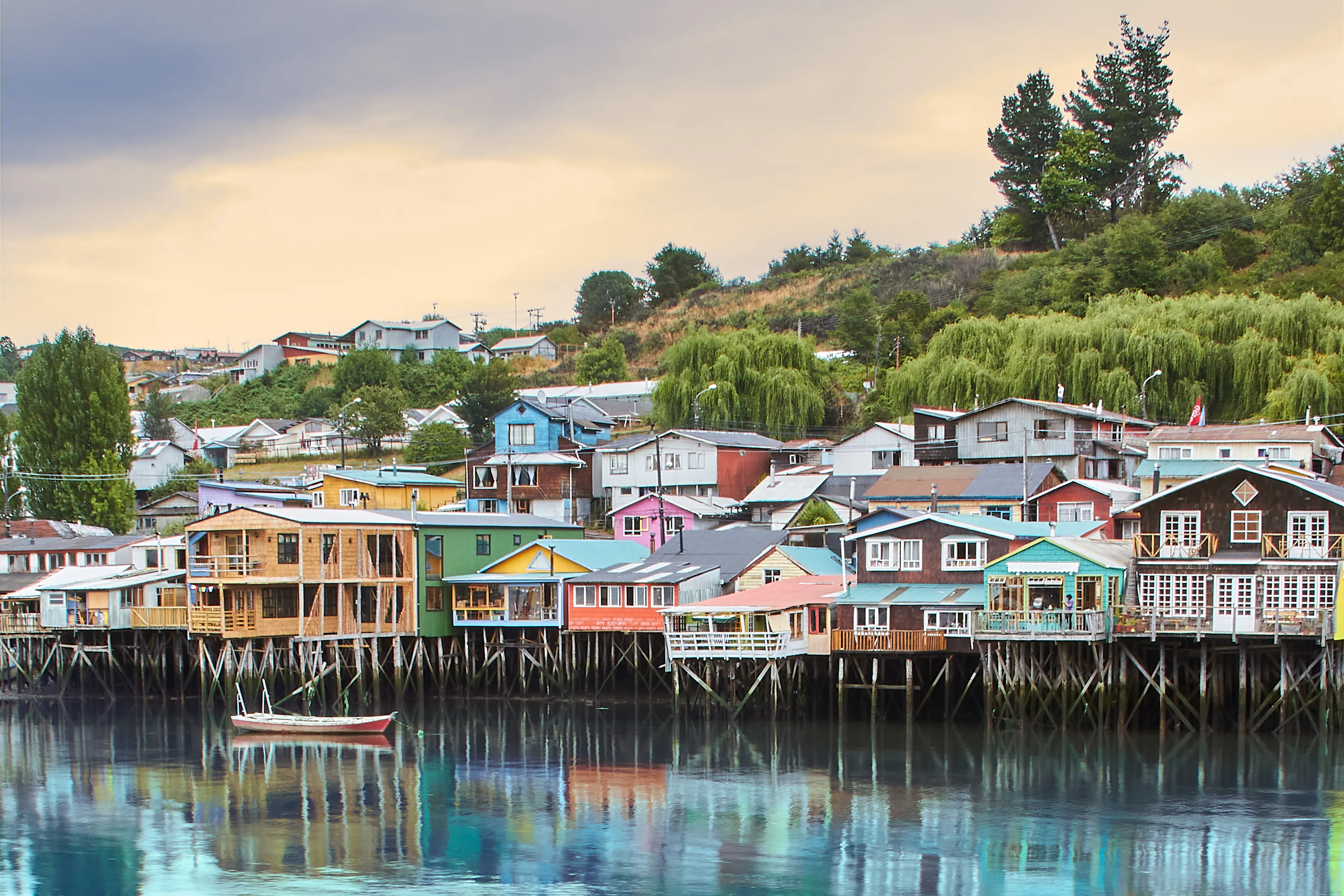 Colorful stilted wooden houses line a waterfront with small boats moored below in southern Chile.