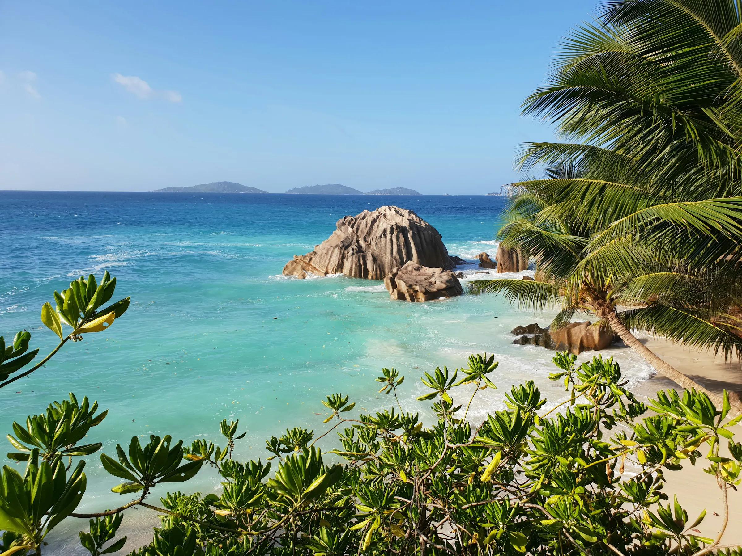 Huge smooth granite boulders frame a turquoise cove with white sand and calm water on La Digue.