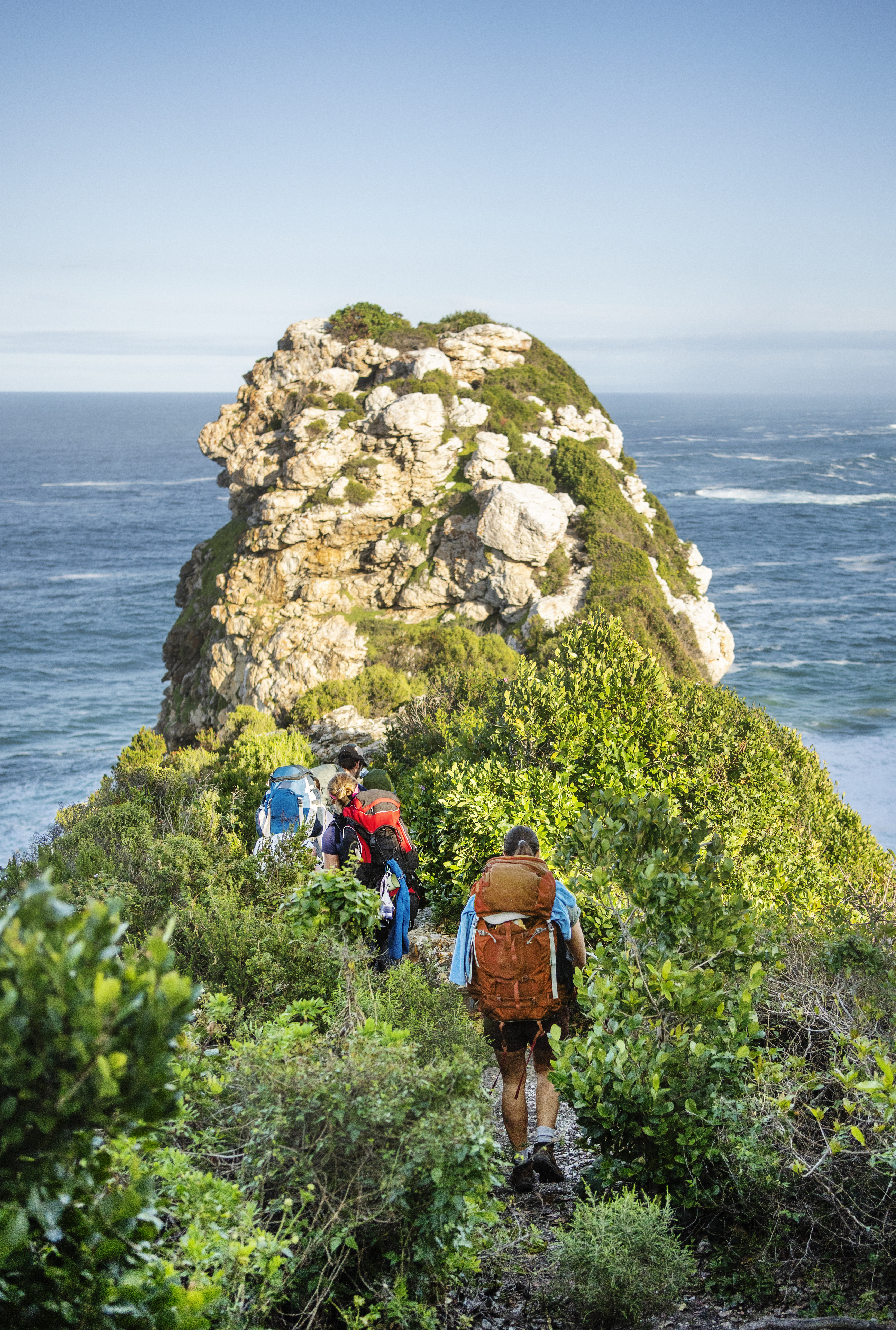 A turquoise coastal bay flanked by green forested headlands and a pebbly beach in South Africa.
