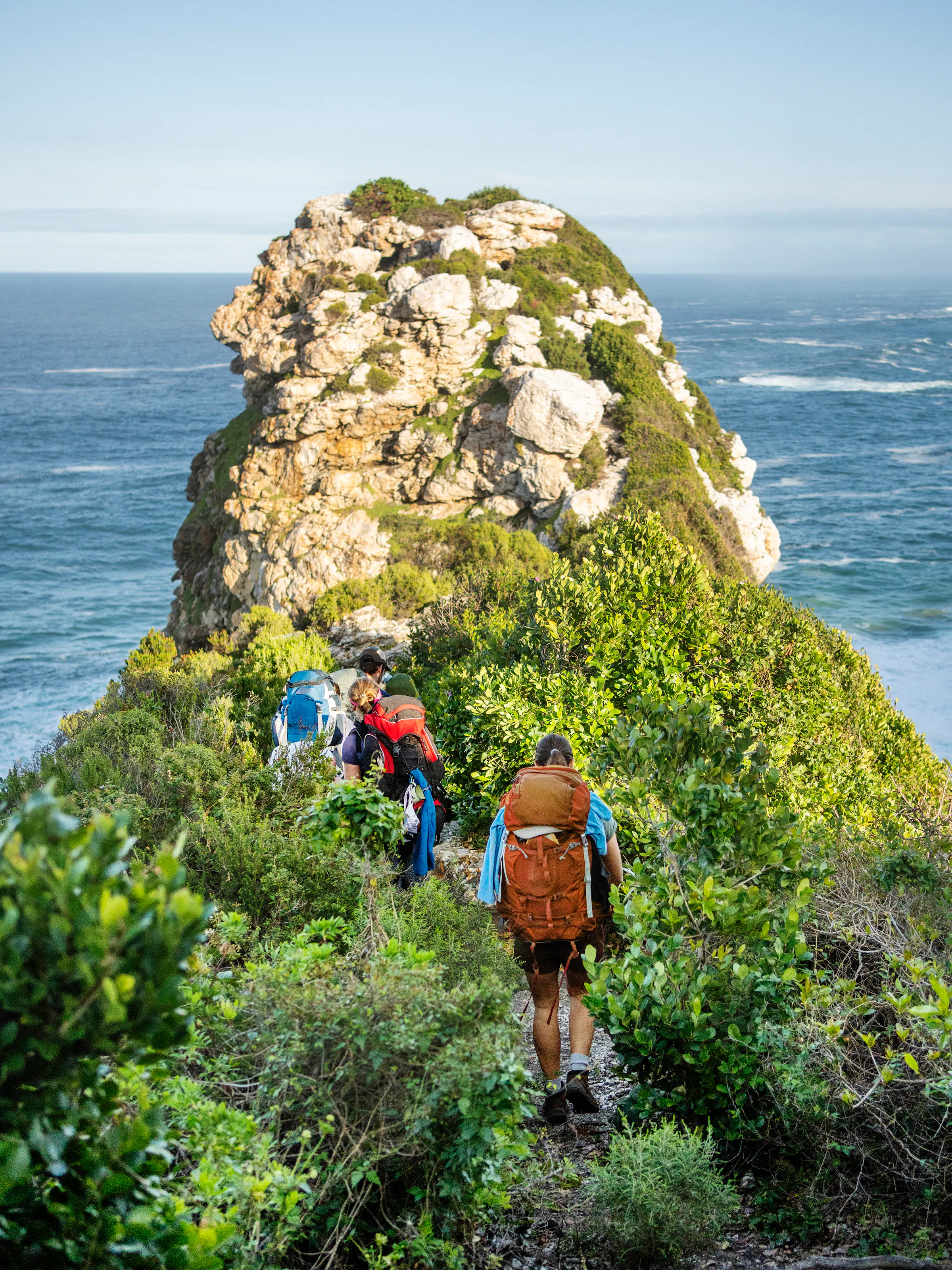 A turquoise coastal bay flanked by green forested headlands and a pebbly beach in South Africa.