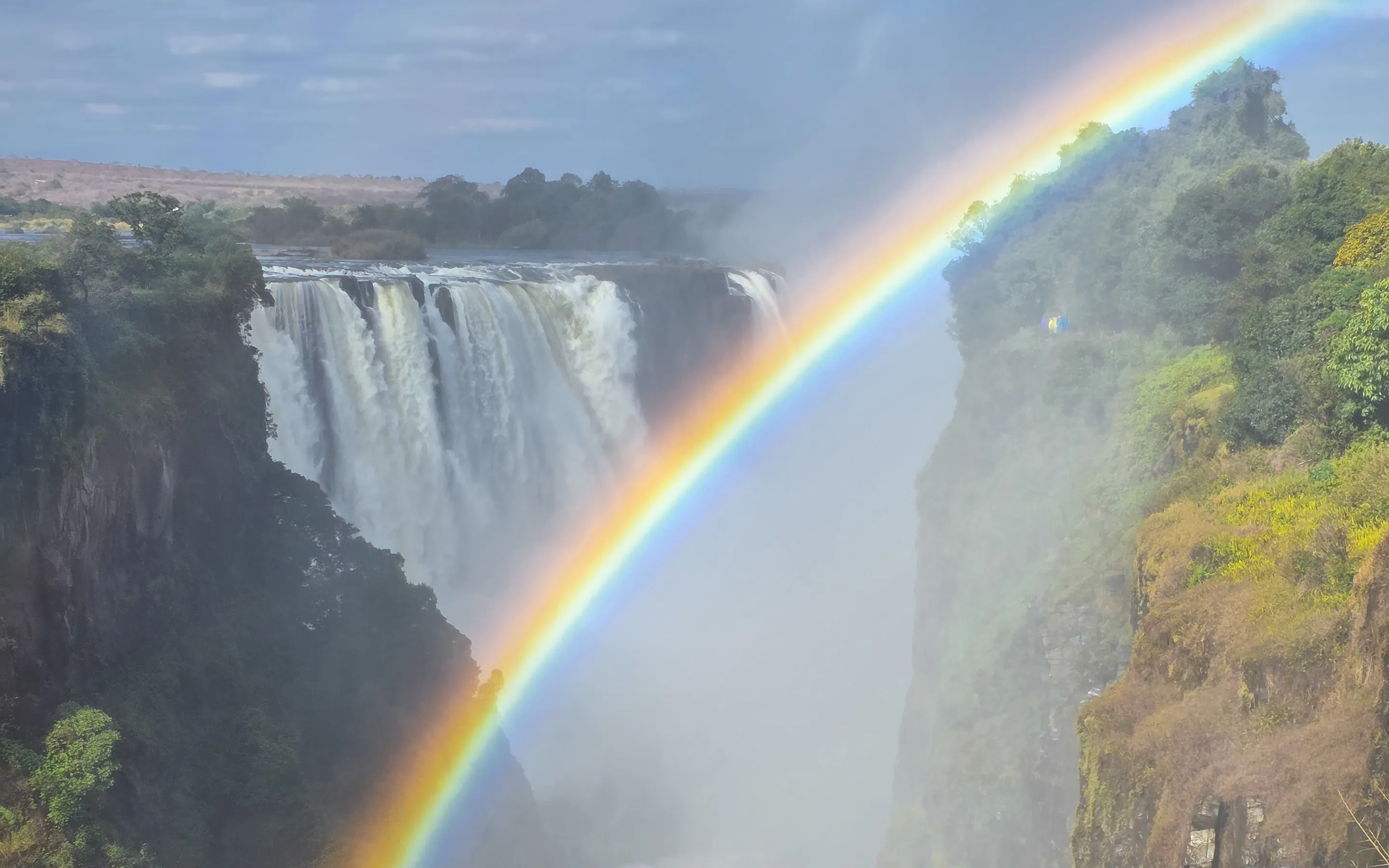 Victoria Falls thunders into a deep gorge beneath a vivid rainbow arching through the mist.