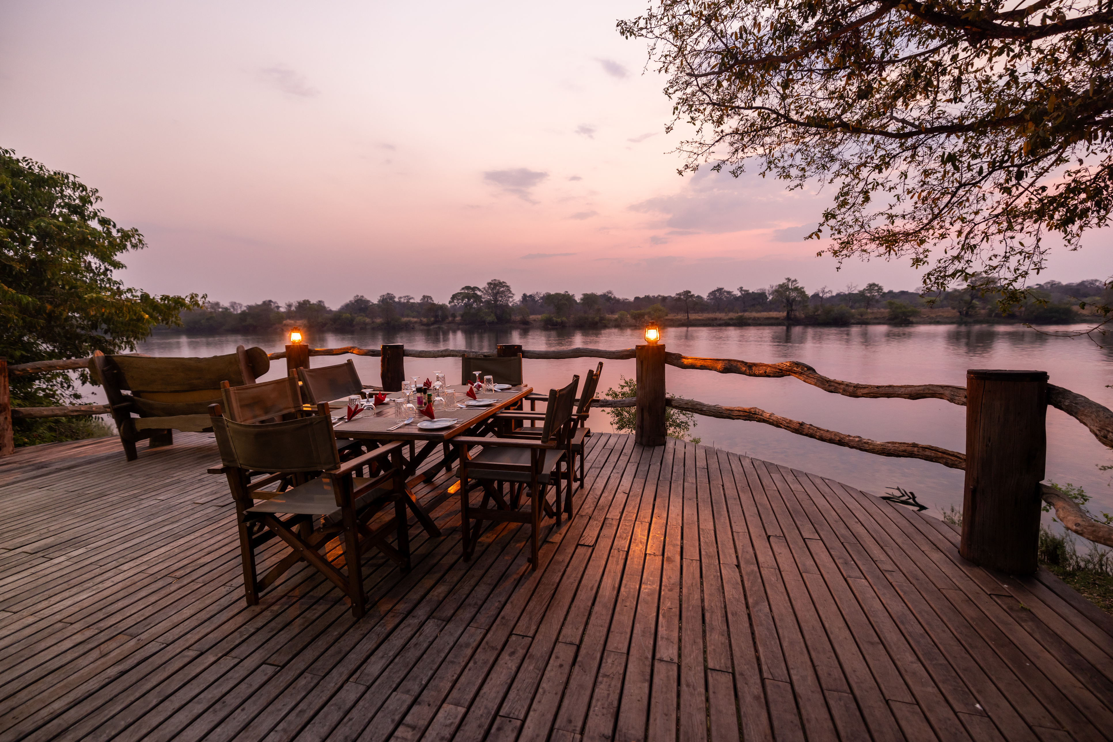 A safari camp deck with chairs and lanterns overlooks open bushveld at dusk in Zambia.