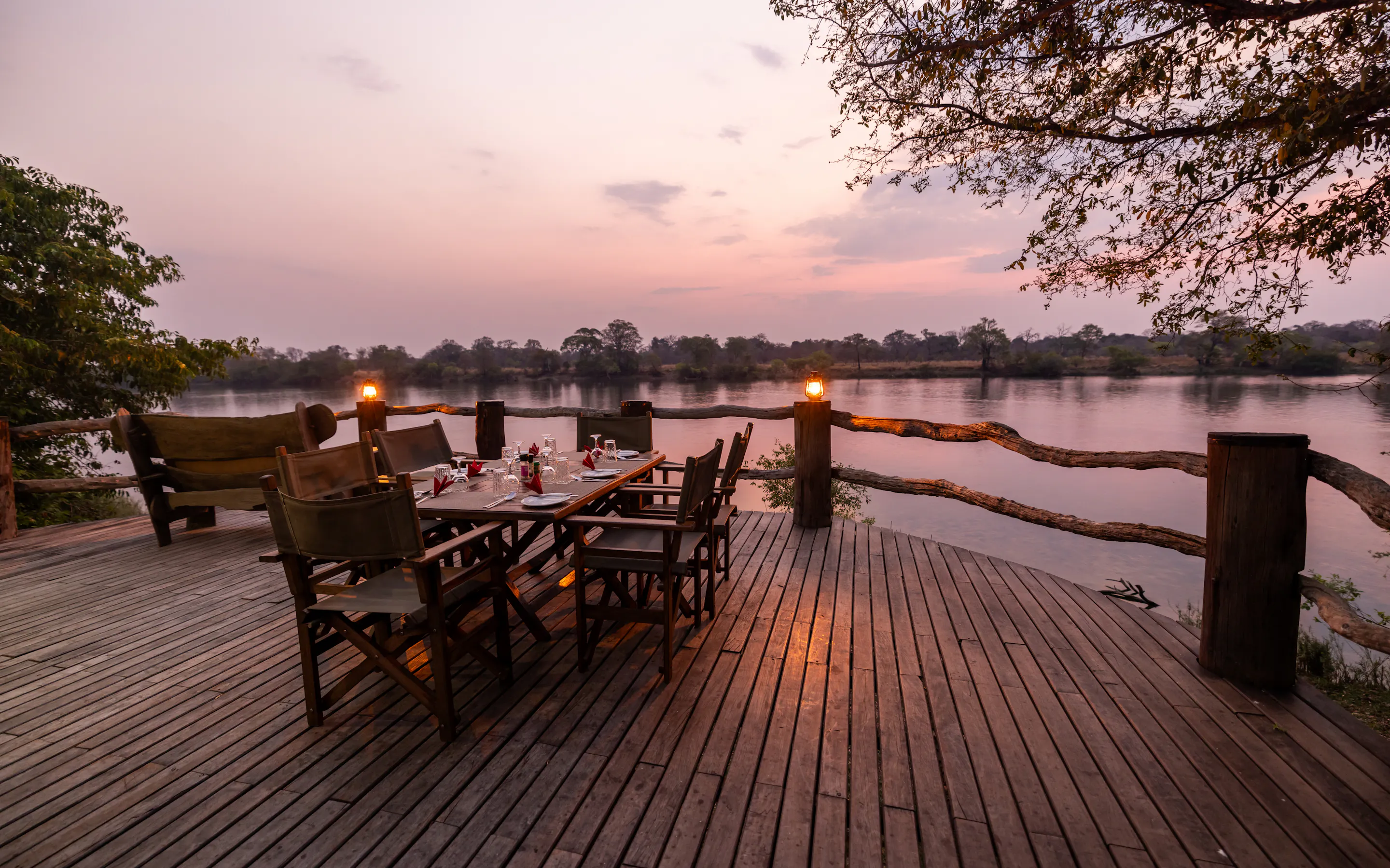 A safari camp deck with chairs and lanterns overlooks open bushveld at dusk in Zambia.