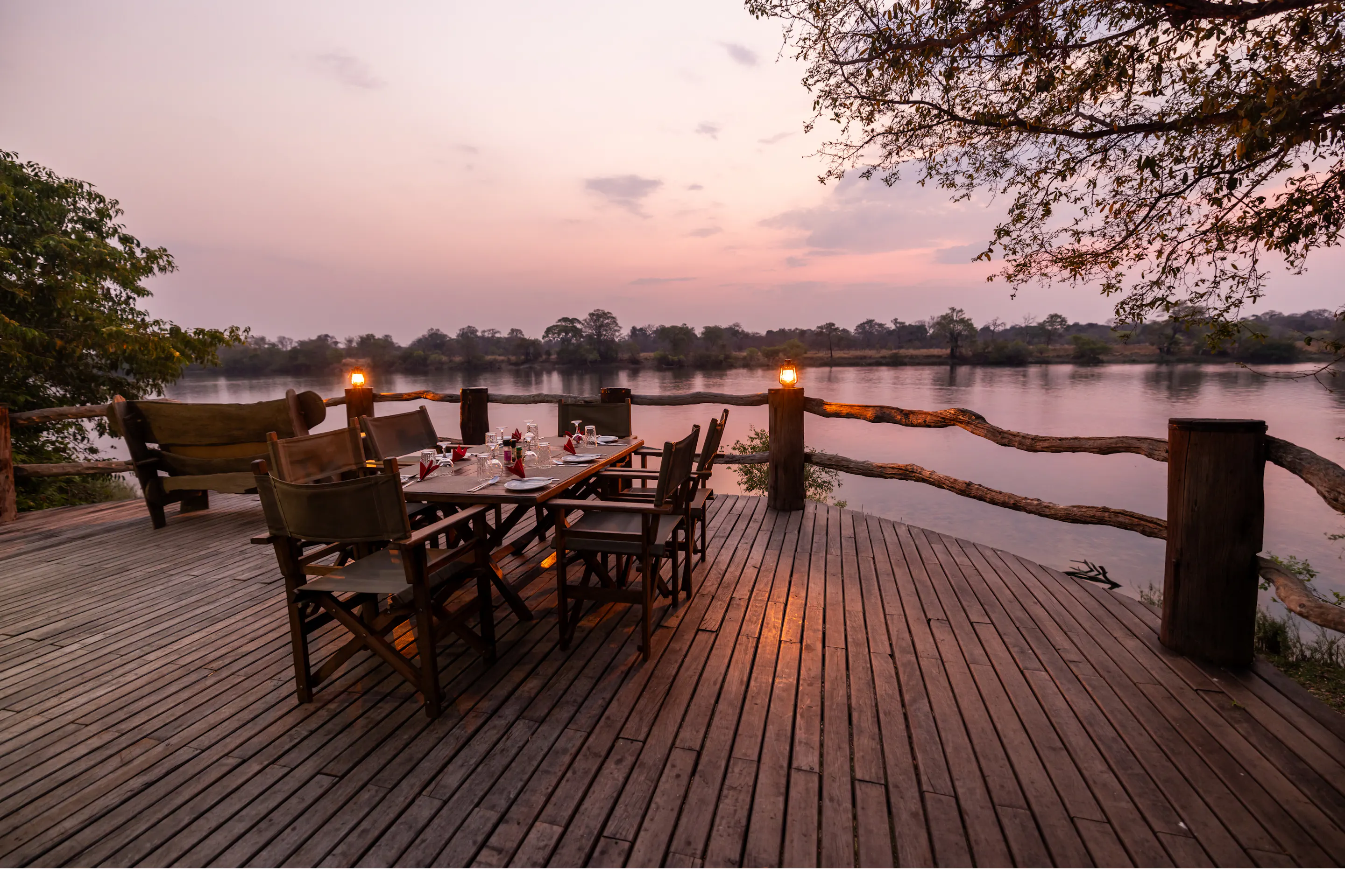 A safari camp deck with chairs and lanterns overlooks open bushveld at dusk in Zambia.