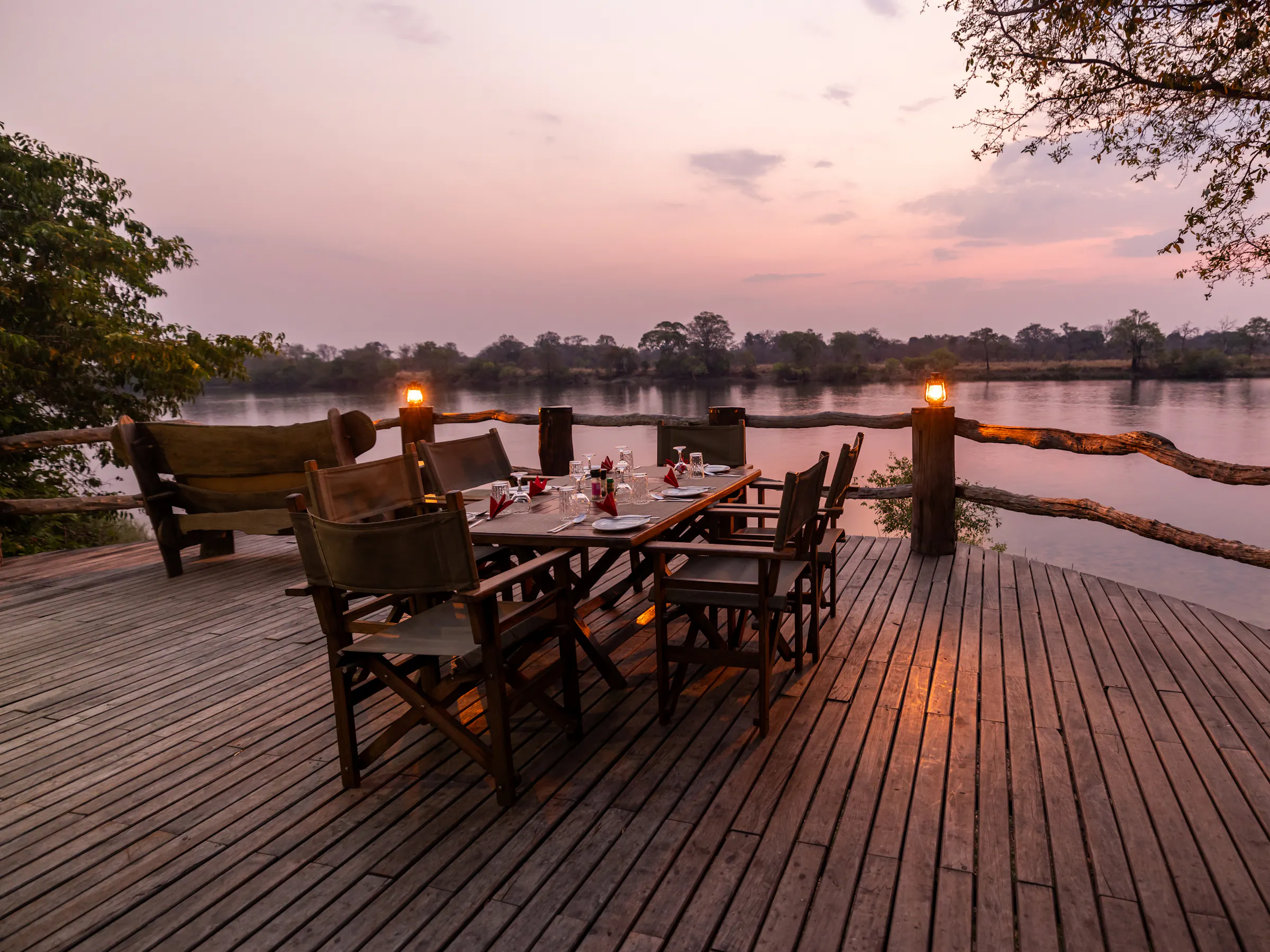 A safari camp deck with chairs and lanterns overlooks open bushveld at dusk in Zambia.