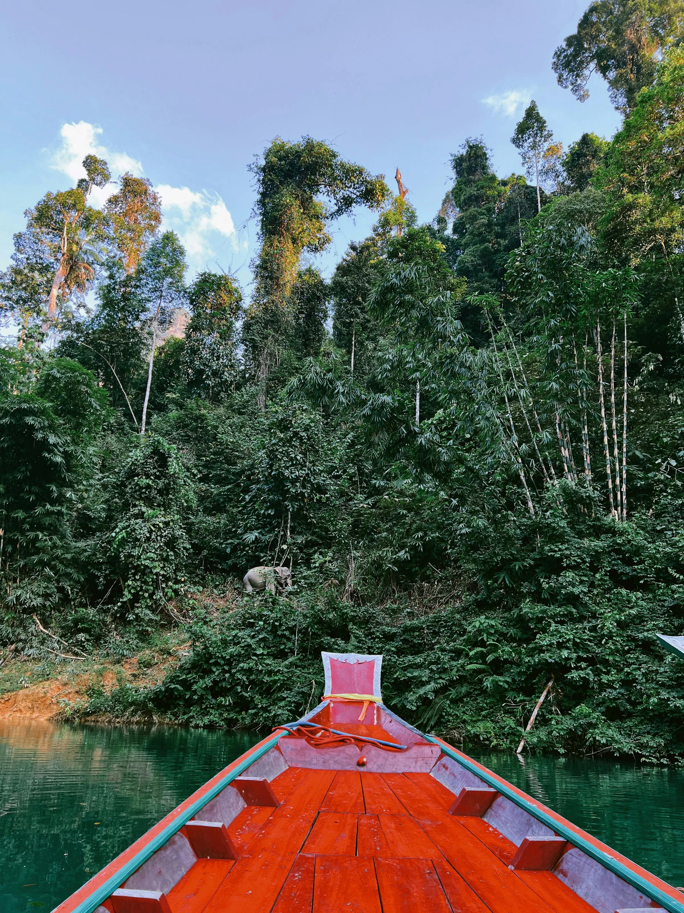 The bow of a red traditional longtail boat points toward forested limestone karst islands.
