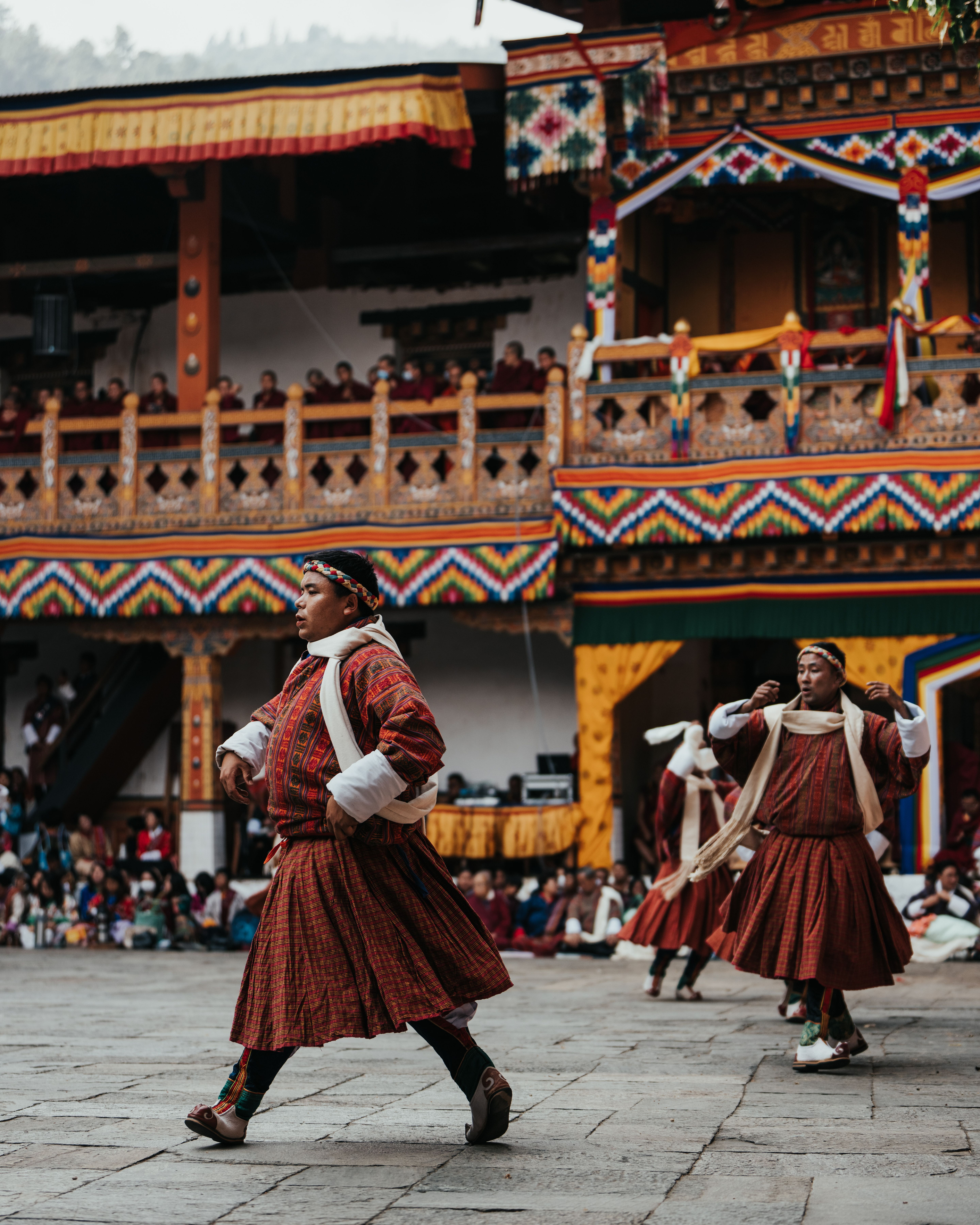 Monks in red and saffron robes perform a traditional dance in an ornate Bhutanese courtyard.