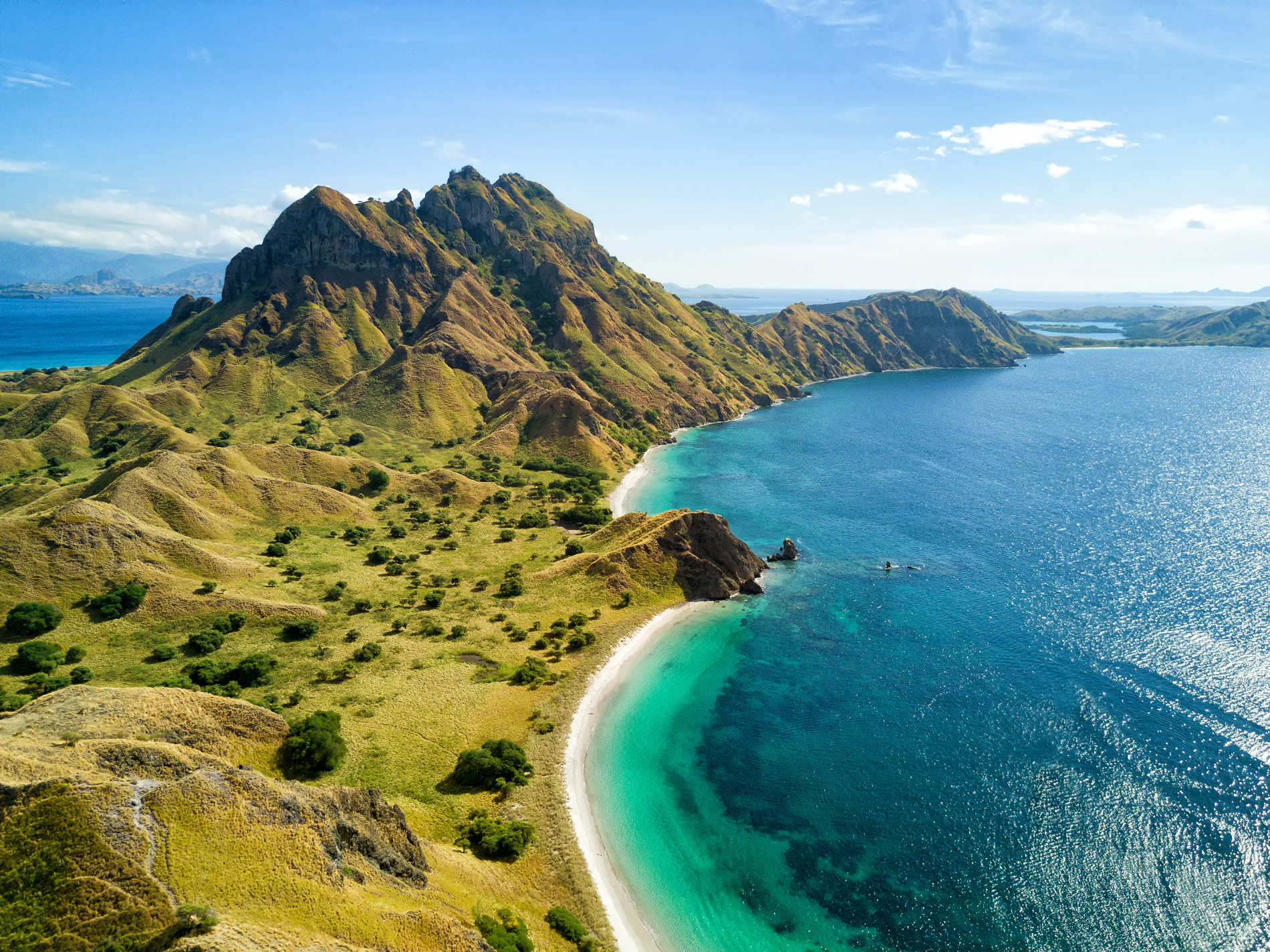 An aerial view of Komodo Island, with large green hills and sandy beaches surrounded by turquoise water. 