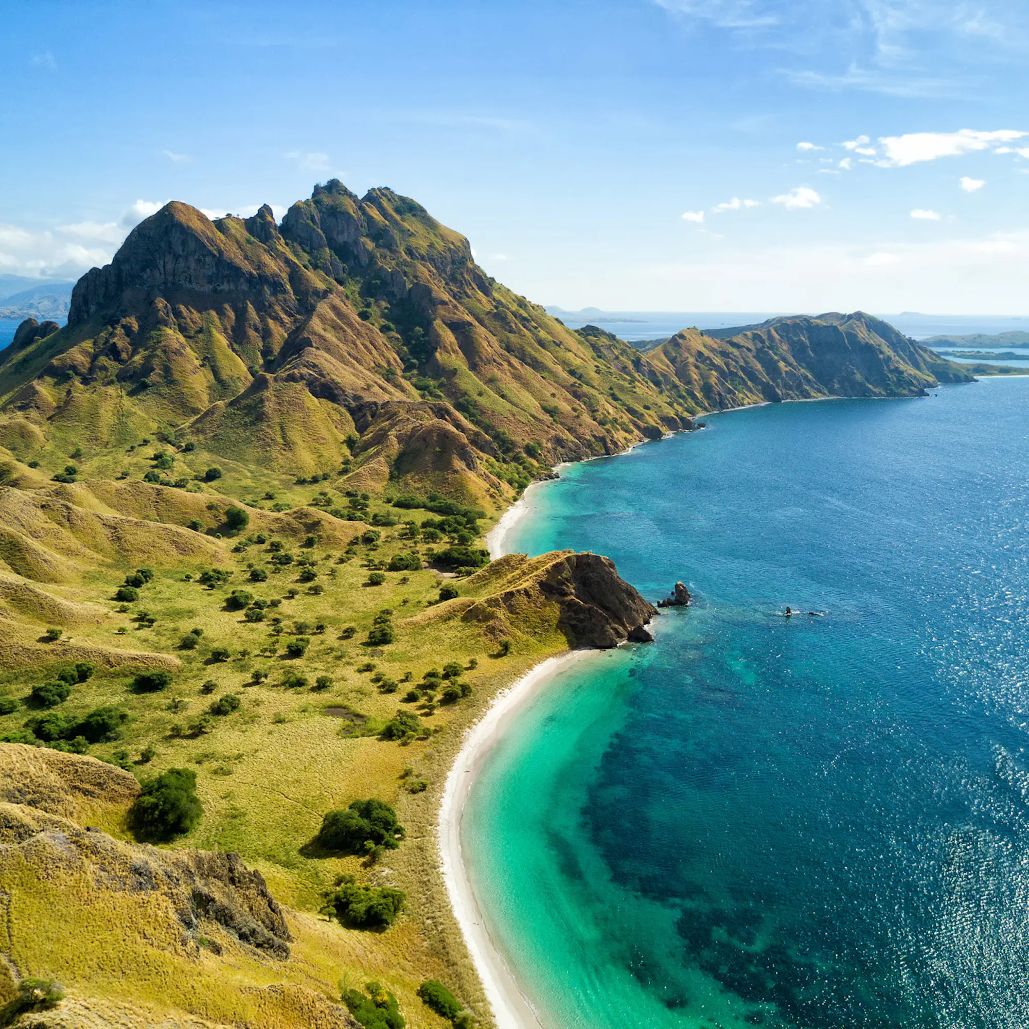 An aerial view of Komodo Island, with large green hills and sandy beaches surrounded by turquoise water.