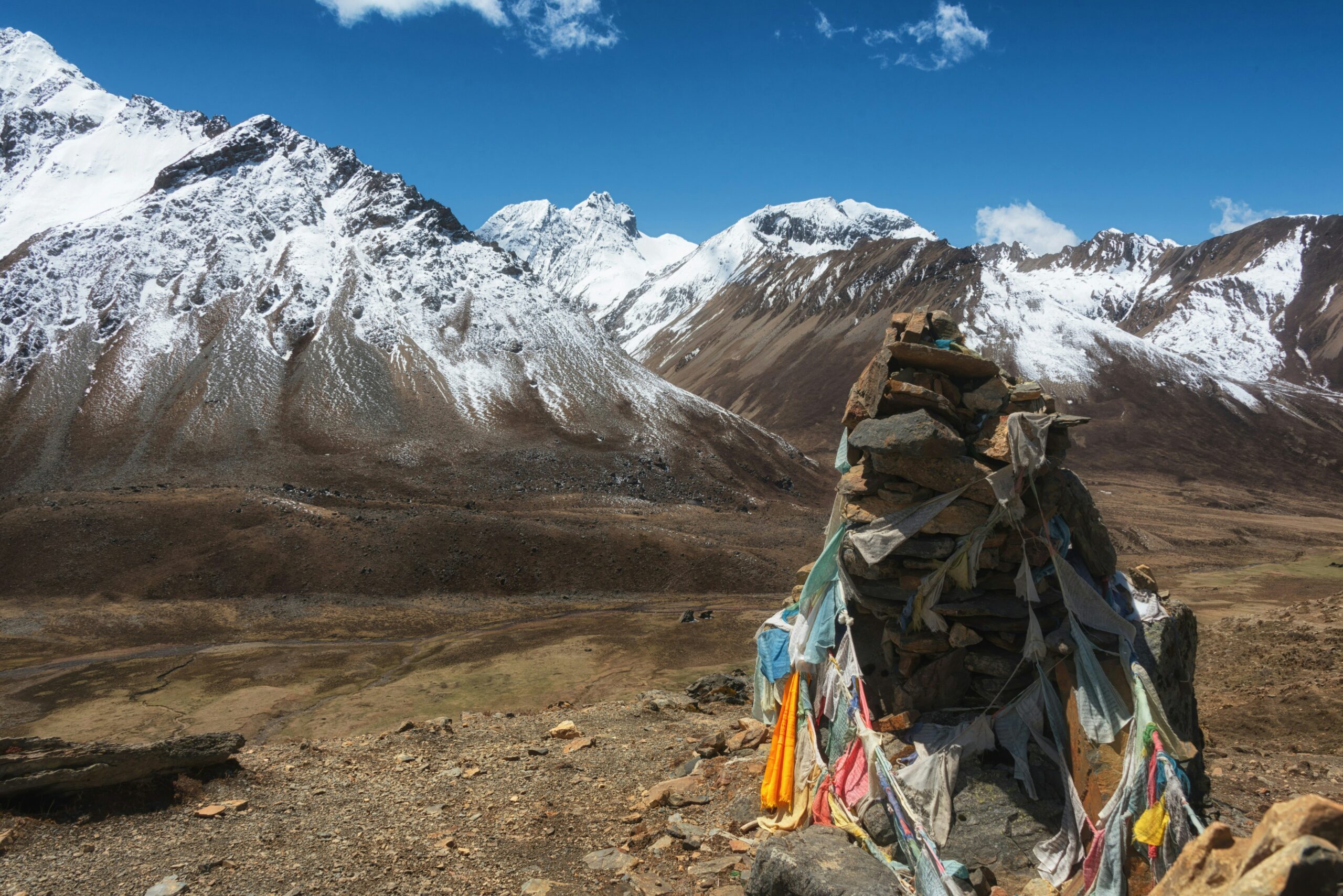 A rock draped with prayer flags sits in front of large snow-covered mountains in Gasa, Bhutan.