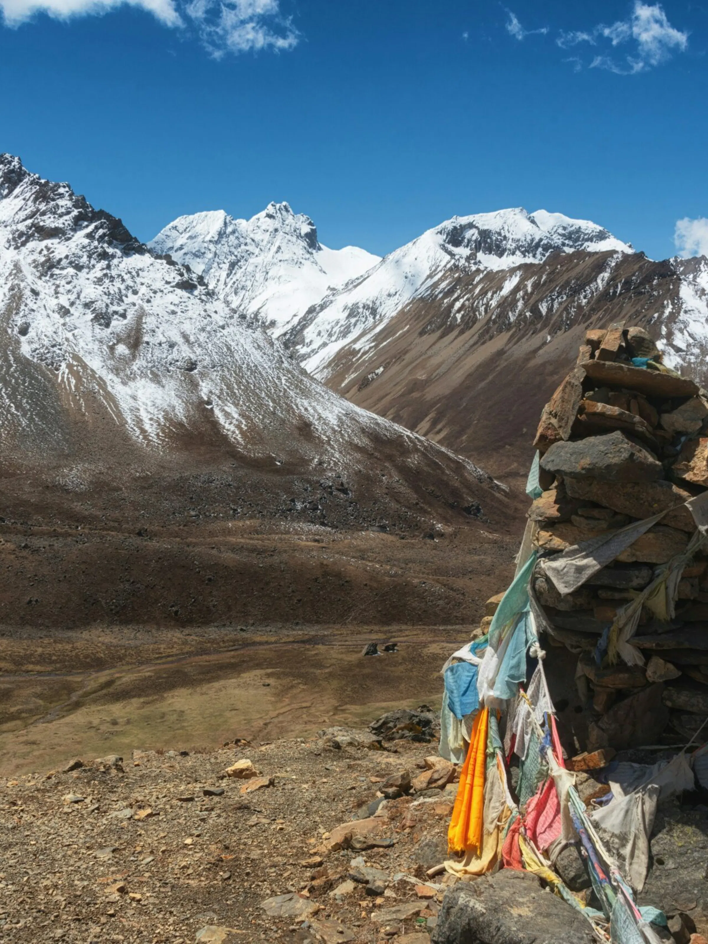 A rock draped with prayer flags sits in front of large snow-covered mountains in Gasa, Bhutan.