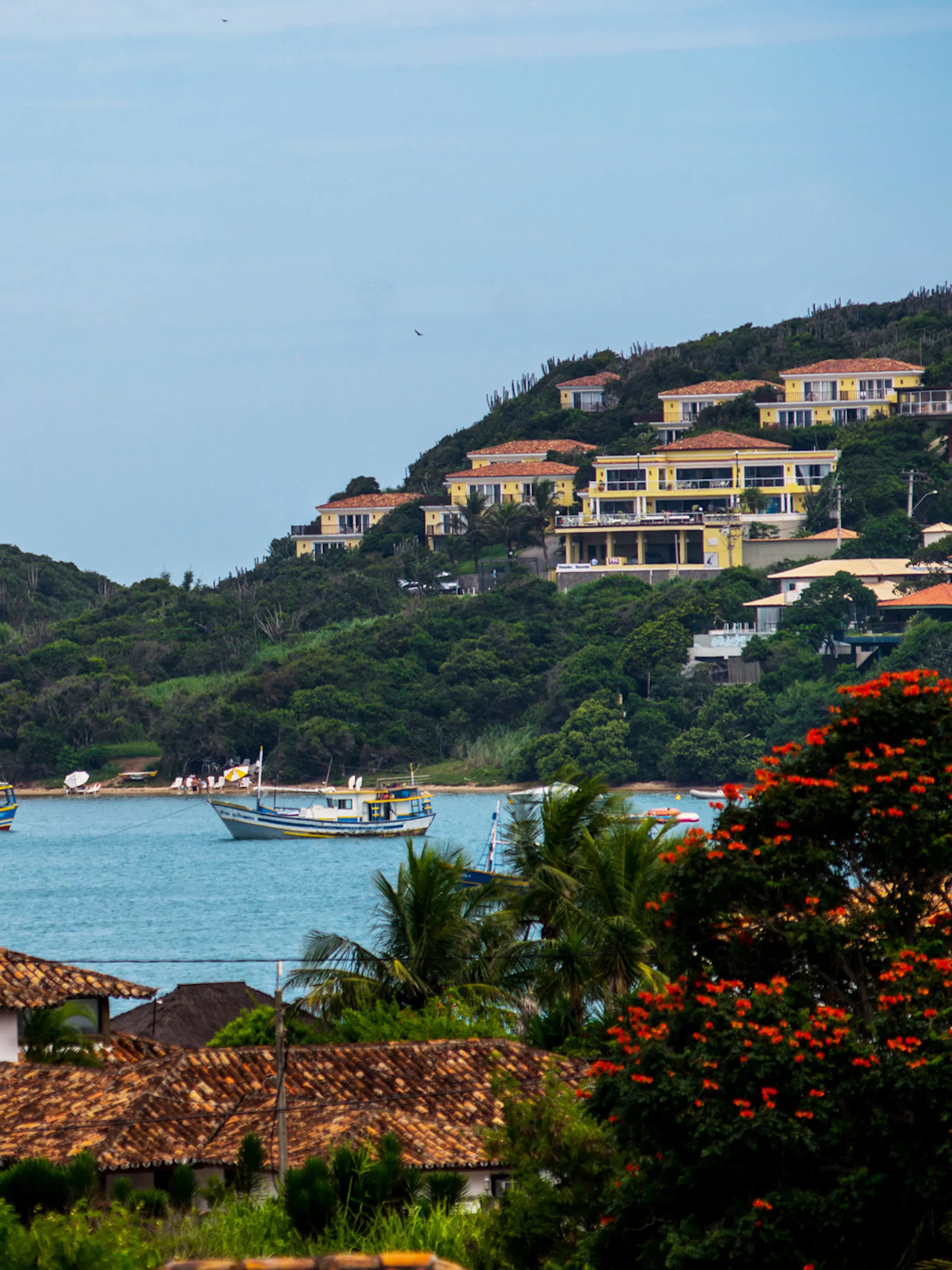 A scenic coastal bay in Brazil's Costa Verde region, featuring several colorful fishing boats moored in calm turquoise water, surrounded by lush green hills.