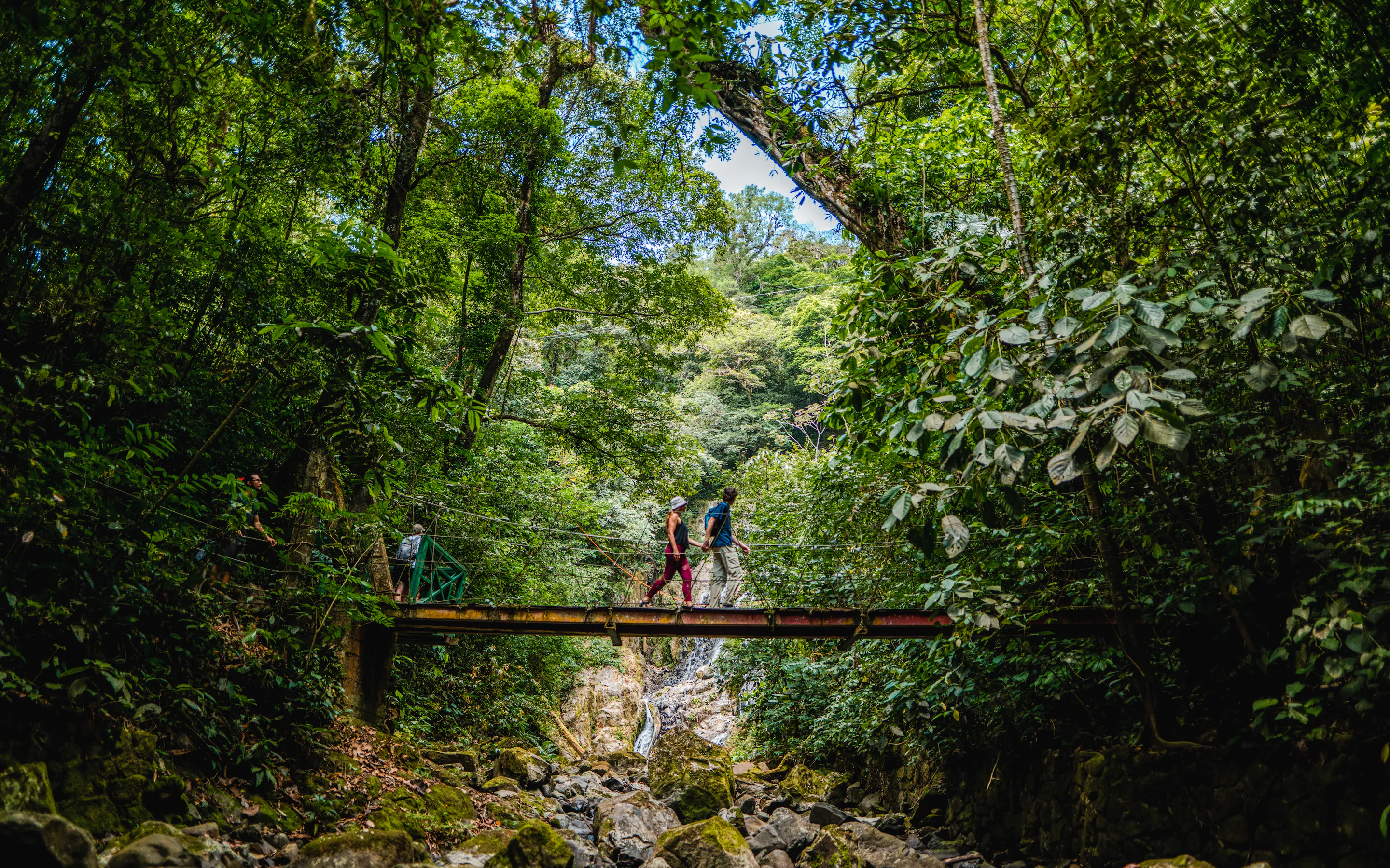 Hikers crossing a suspension bridge above a waterfall on the Sendero Chorro El Macho trail in Valle de Antón, Panama
