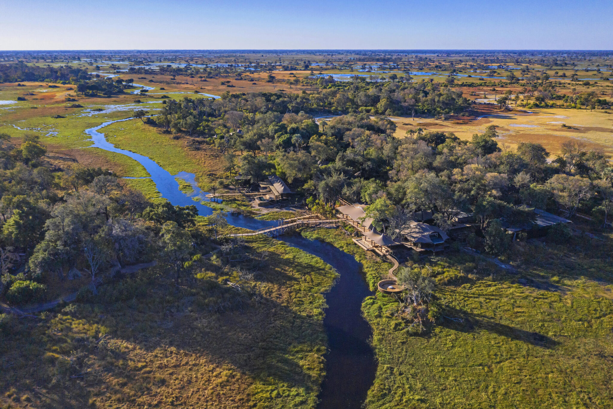 Aerial view of Xigera Camp nestled among trees along a winding channel in the Okavango Delta.