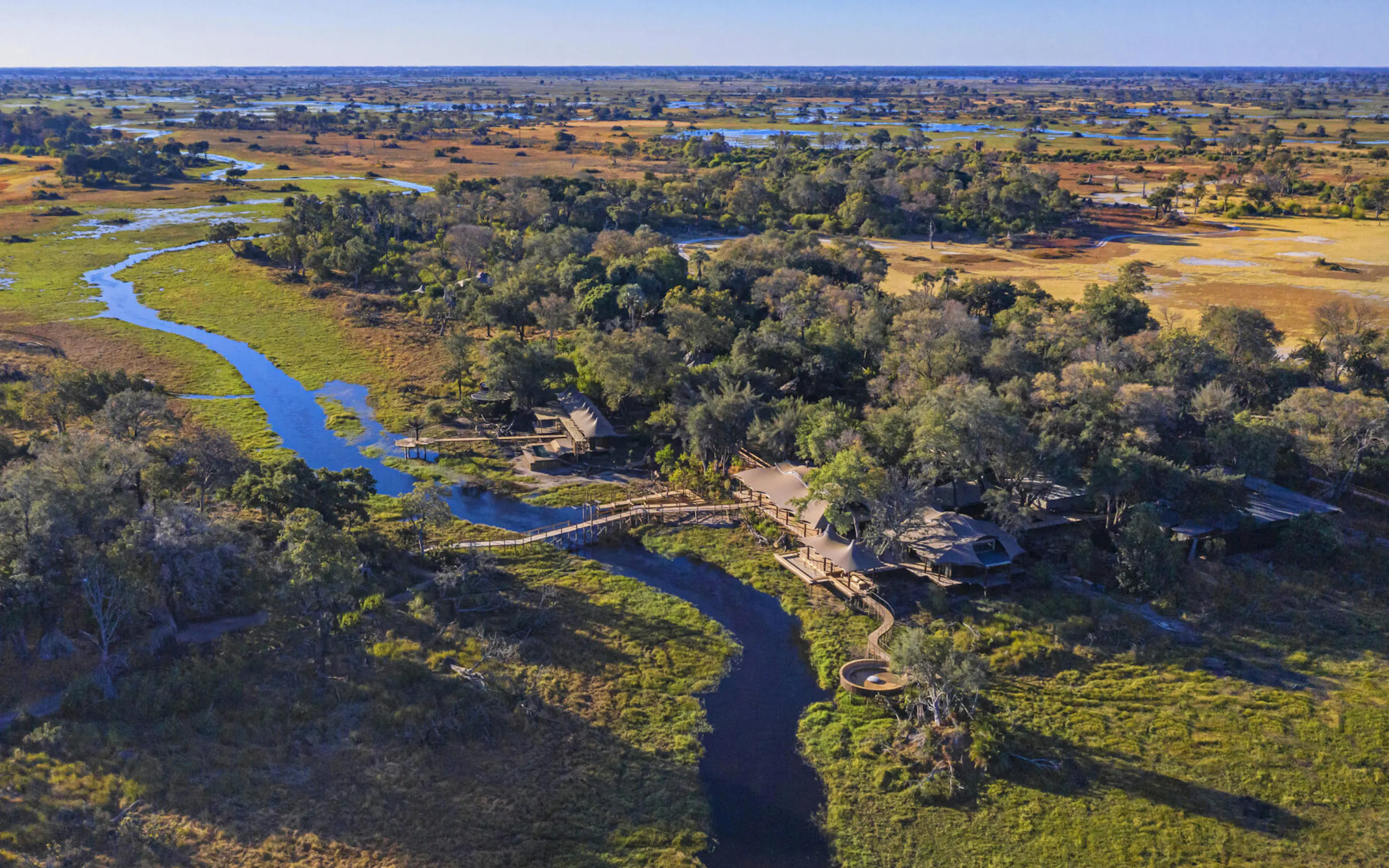 Aerial view of Xigera Camp nestled among trees along a winding channel in the Okavango Delta.