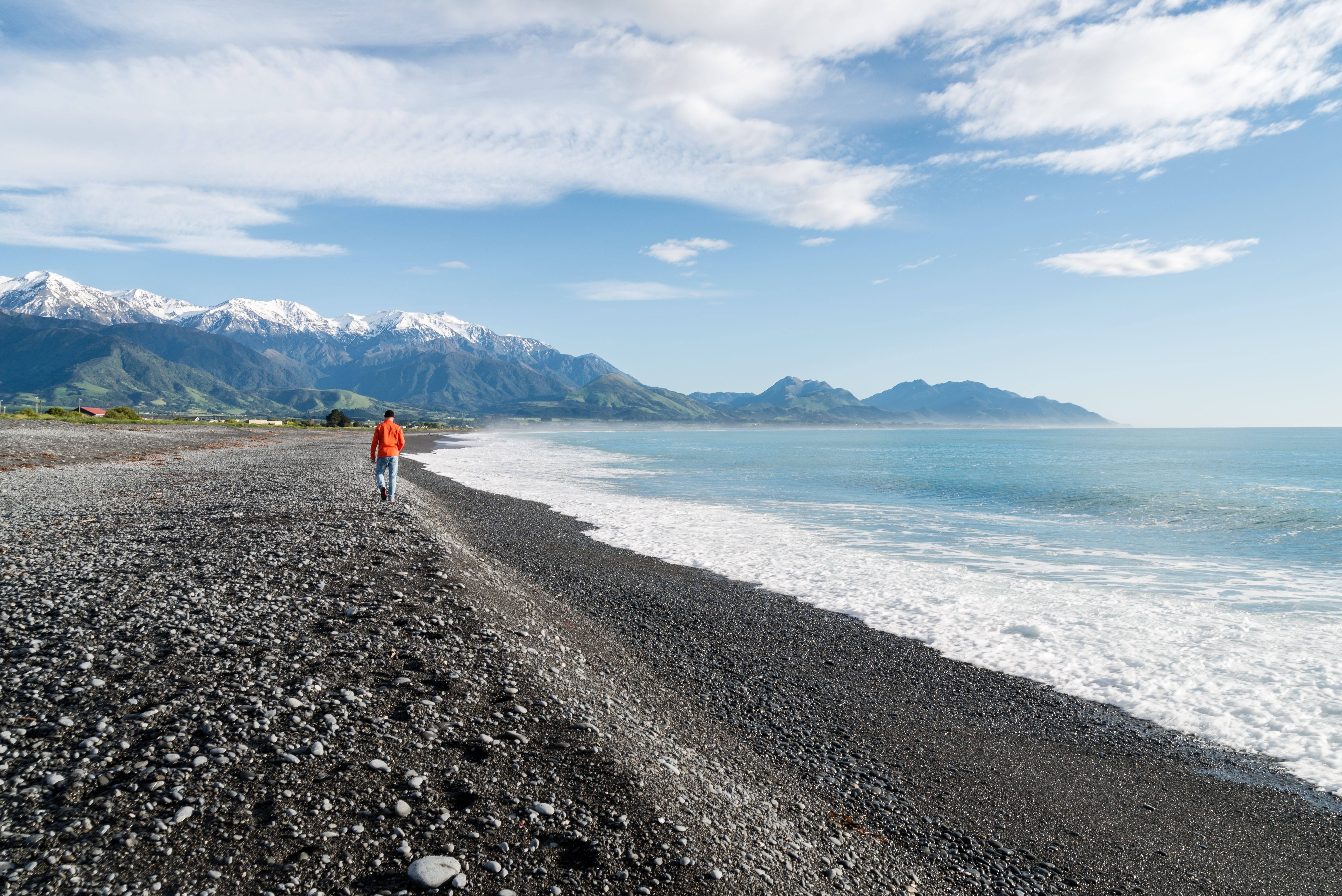 Person walking along the pebble beach with snow-capped mountains in Kaikōura, New Zealand