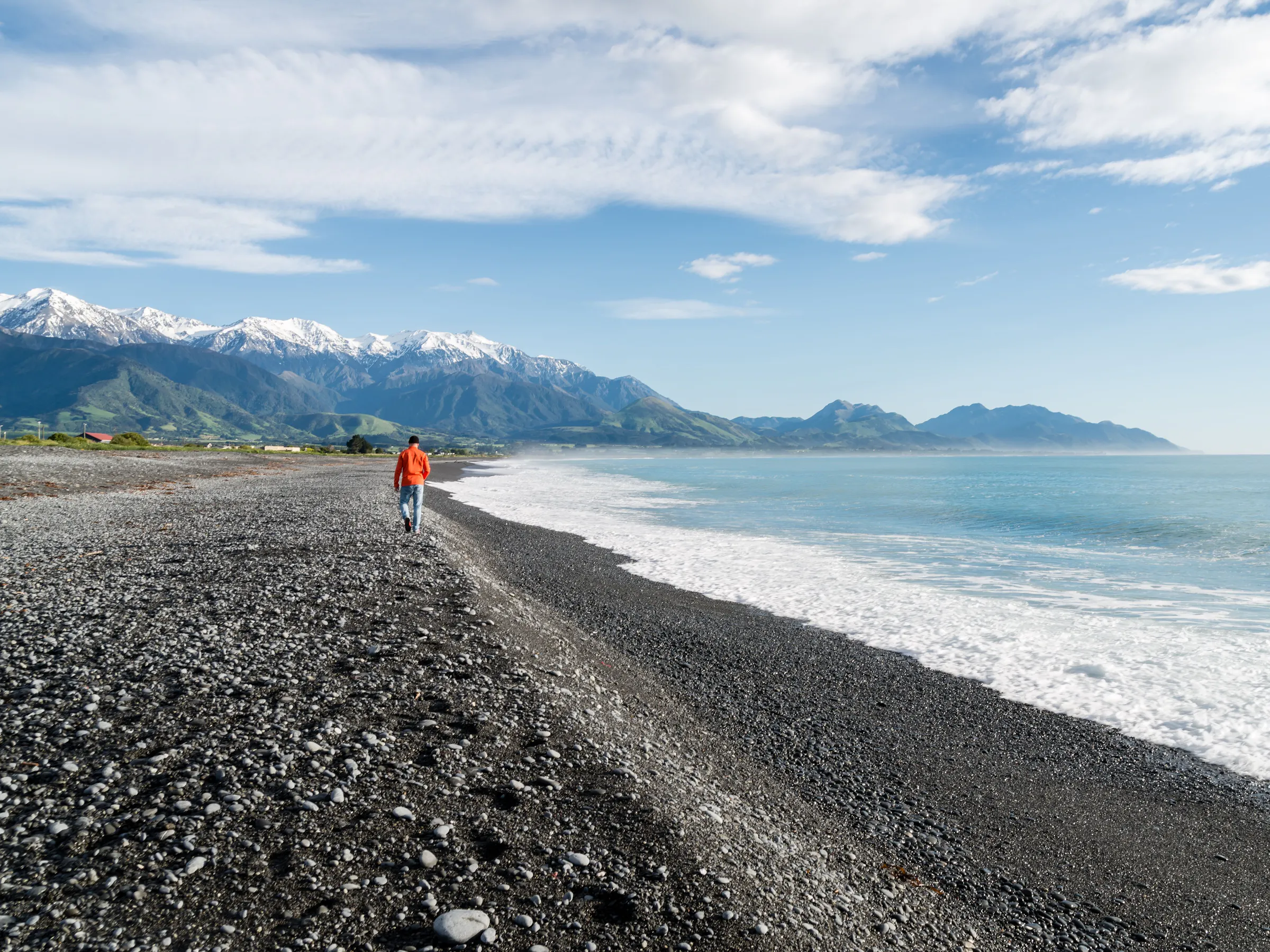 Person walking along the pebble beach with snow-capped mountains in Kaikōura, New Zealand