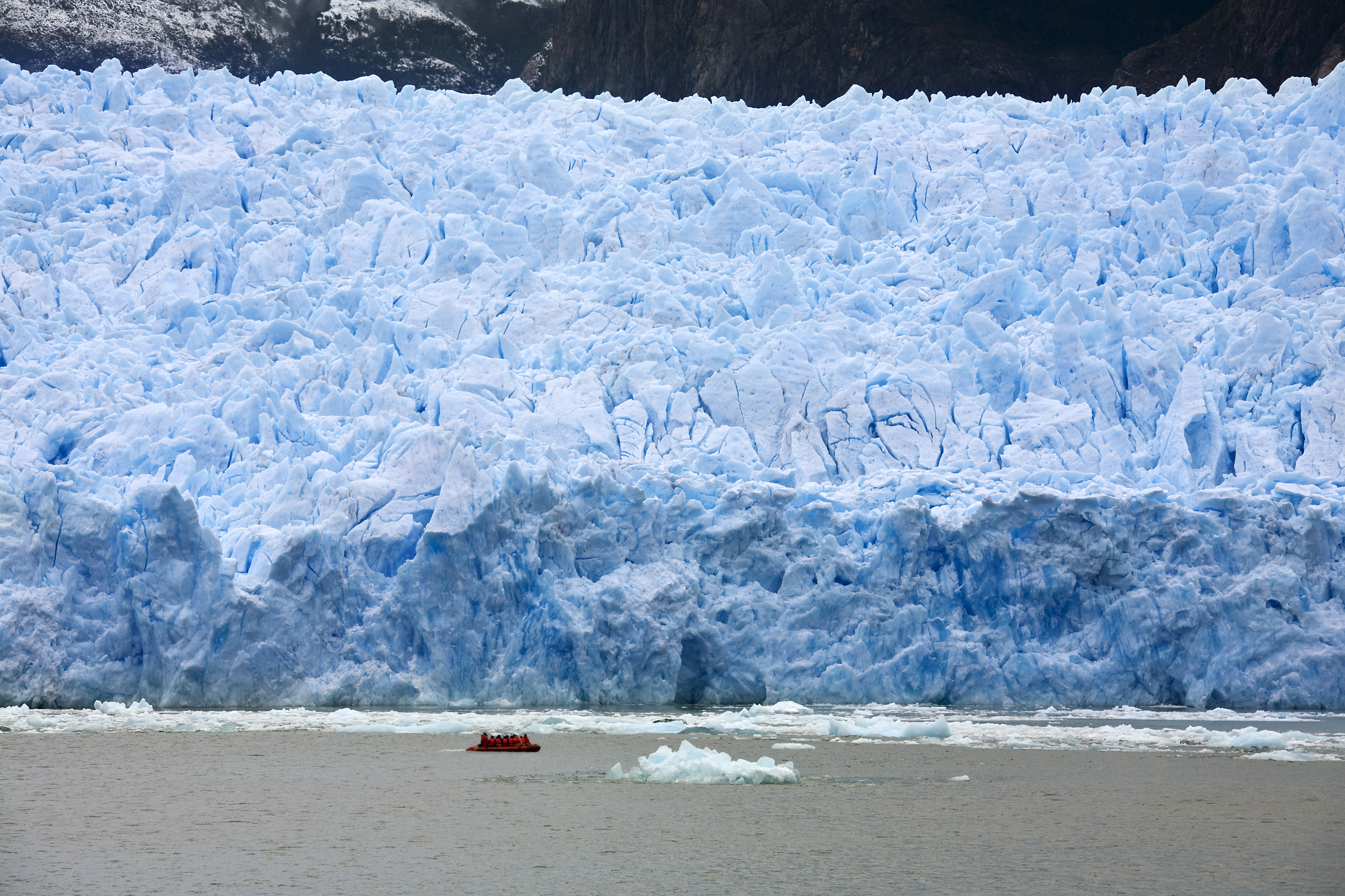 Small boat approaching a massive tabular glacier wall in Aysén, Chile