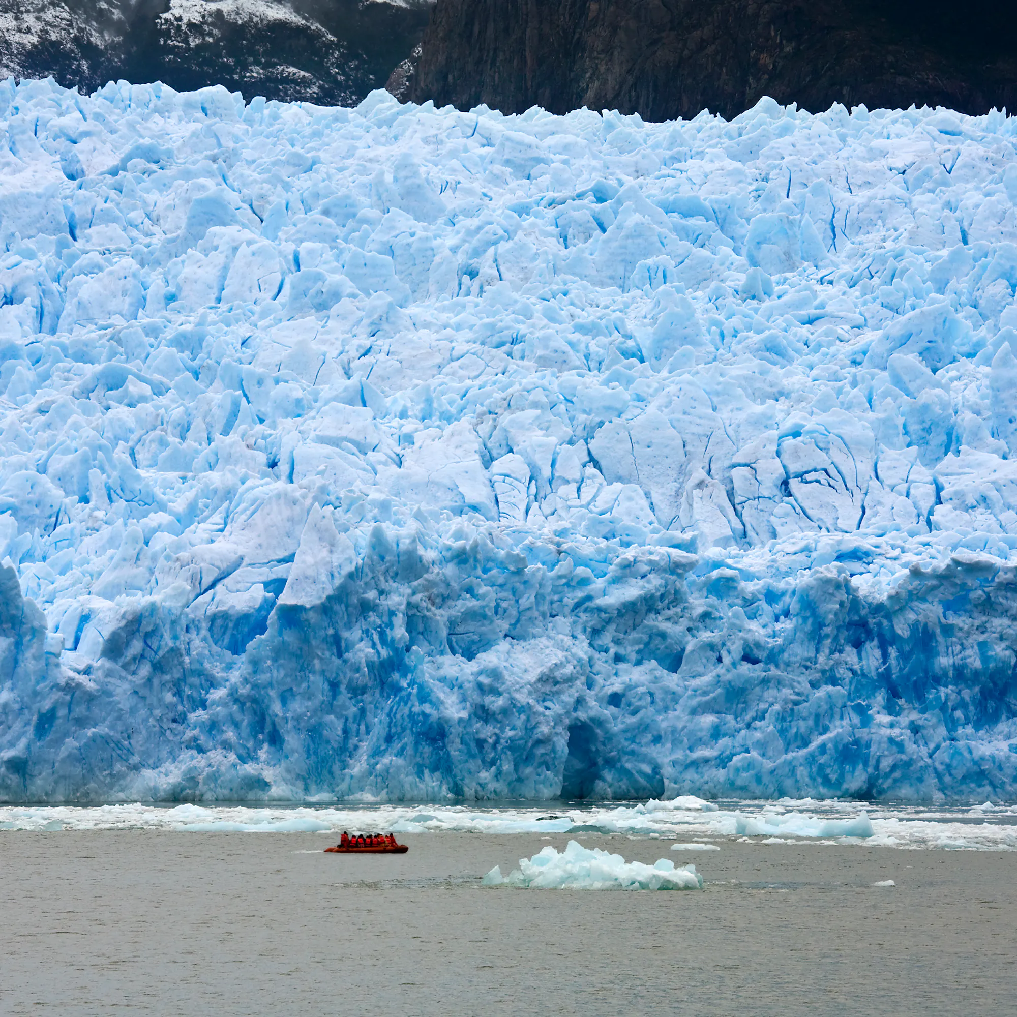 Small boat approaching a massive tabular glacier wall in Aysén, Chile