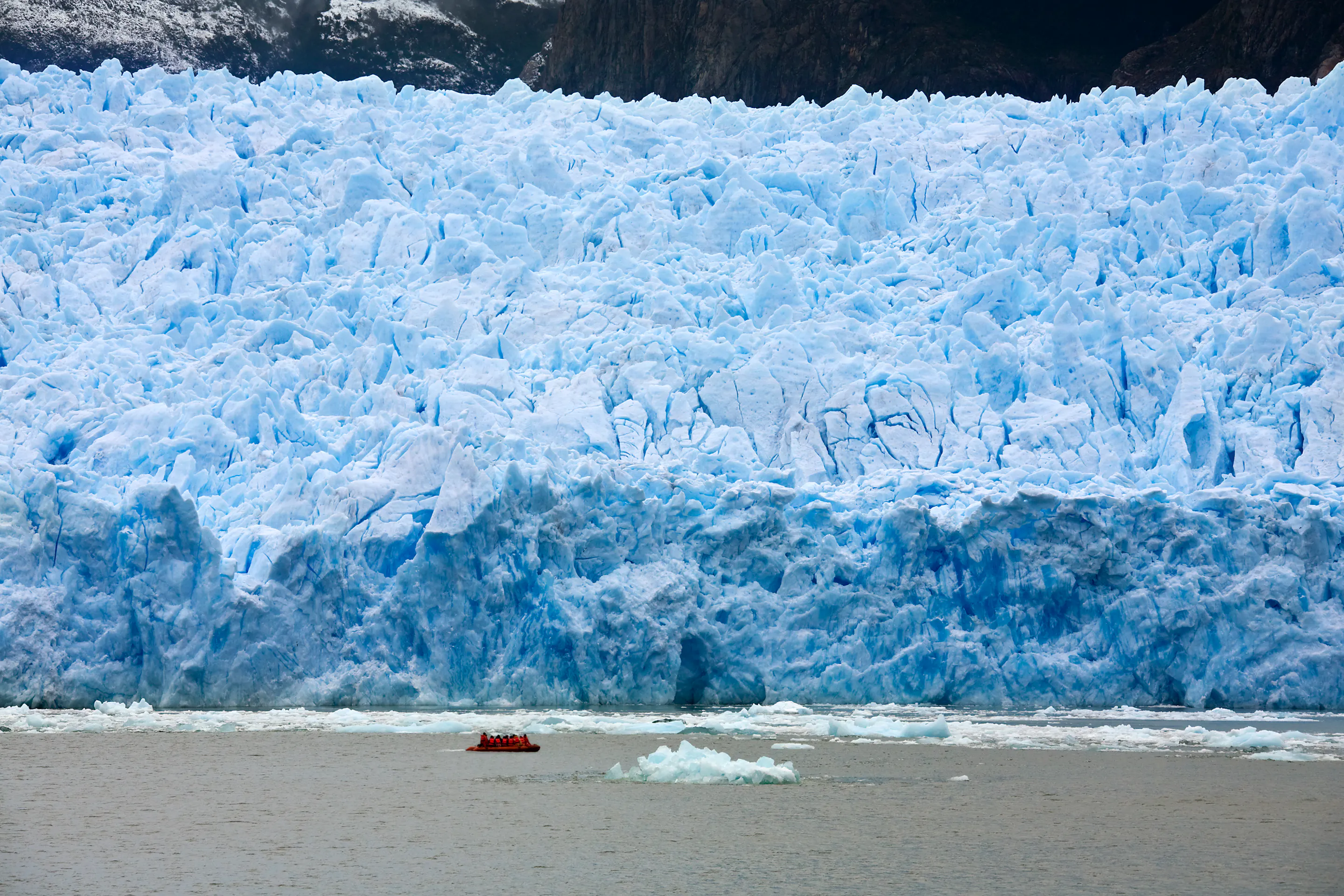 Small boat approaching a massive tabular glacier wall in Aysén, Chile