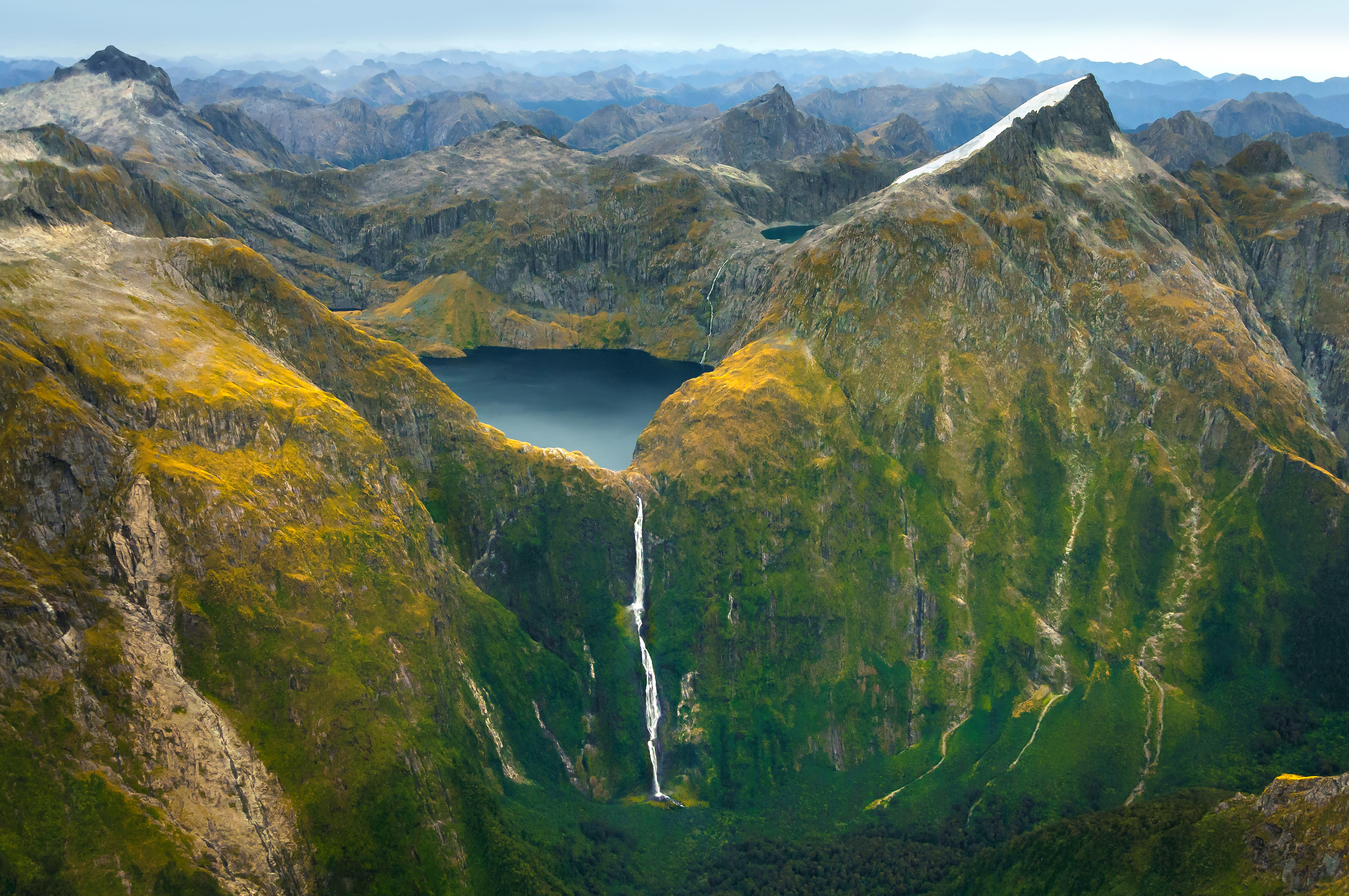 Aerial view of a waterfall and lake in the mountains of Fiordland National Park, New Zealand