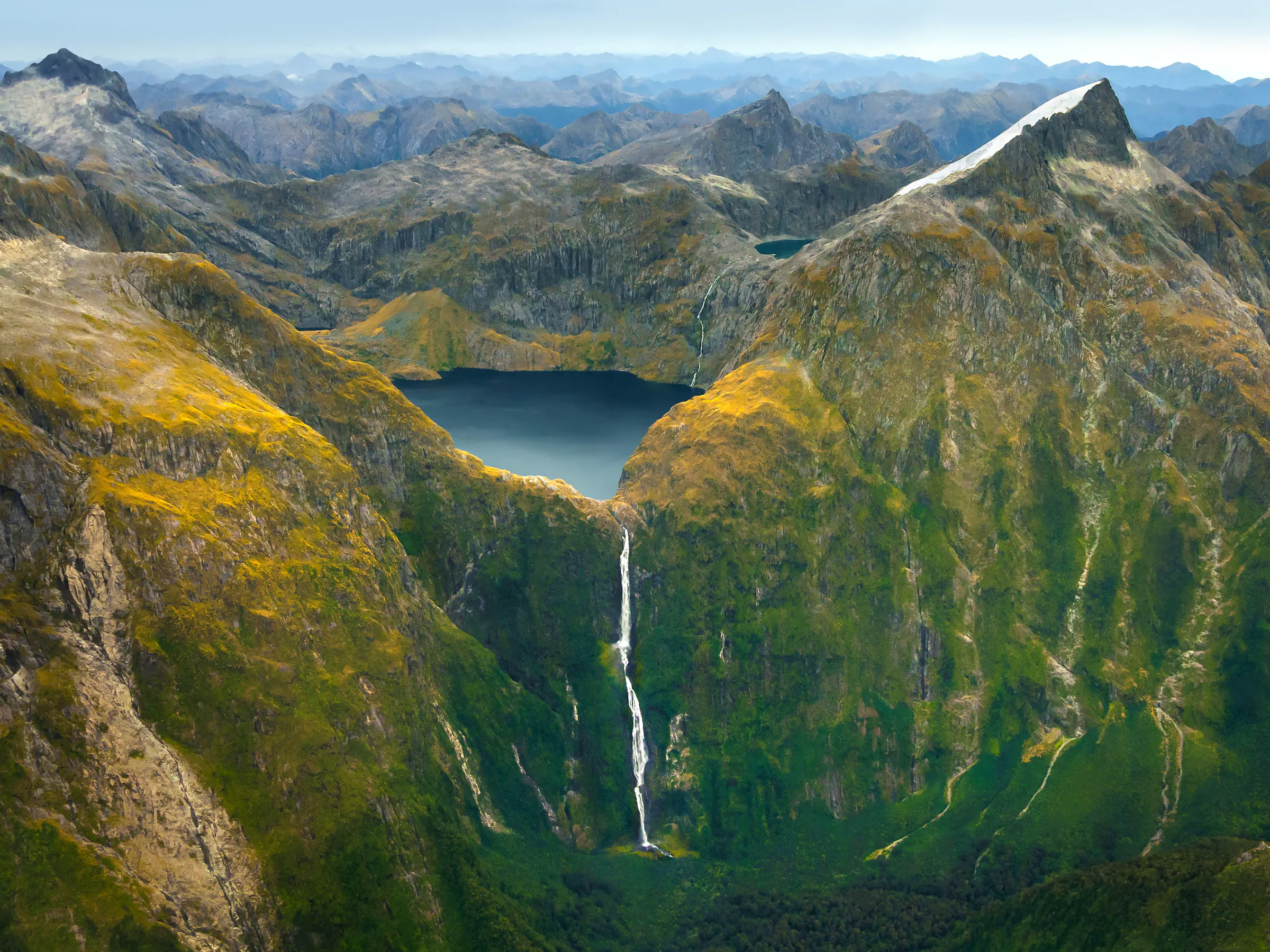 Aerial view of a waterfall and lake in the mountains of Fiordland National Park, New Zealand