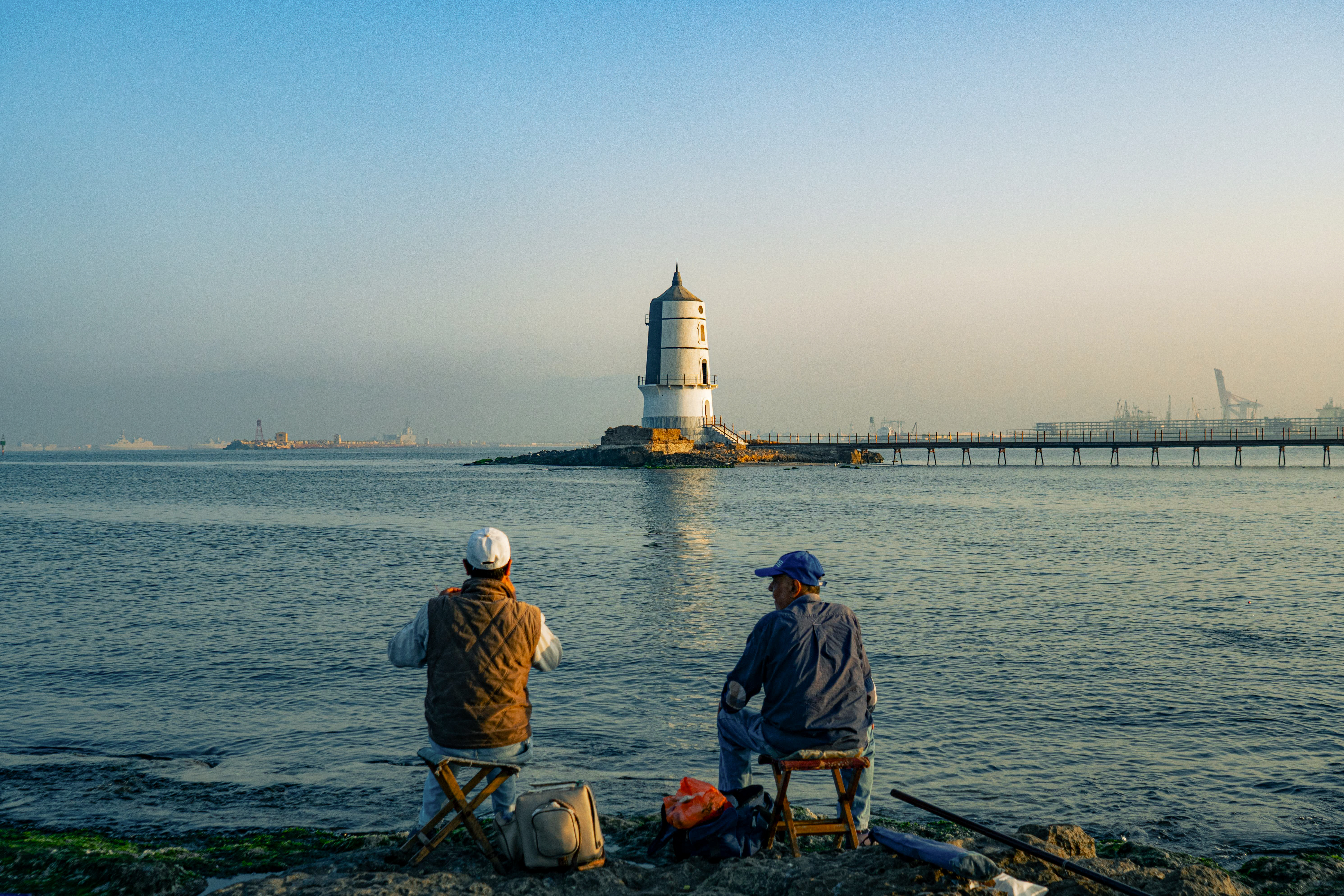 Men fishing on the rocky shore facing a lighthouse in Alexandria harbor, Egypt