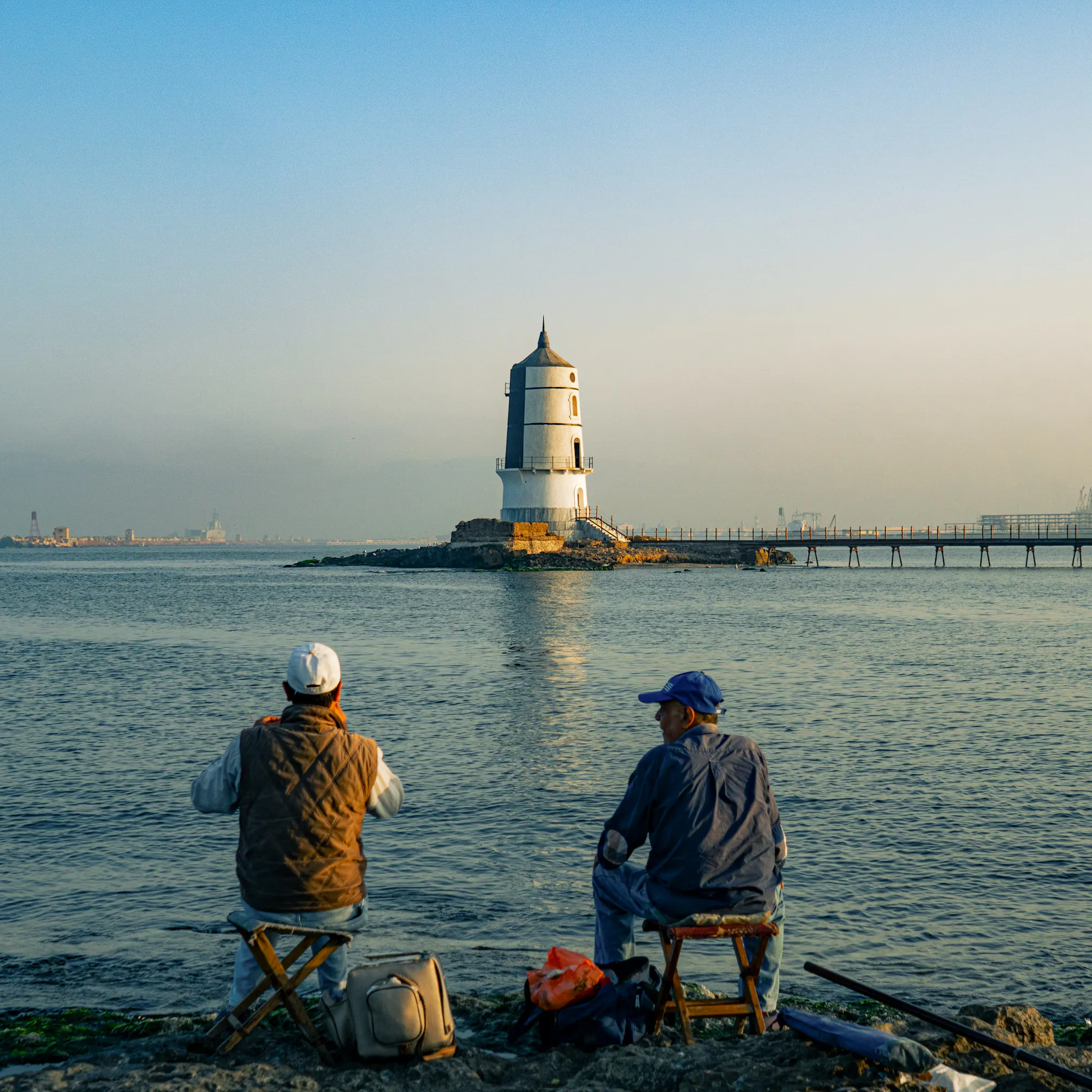 Men fishing on the rocky shore facing a lighthouse in Alexandria harbor, Egypt