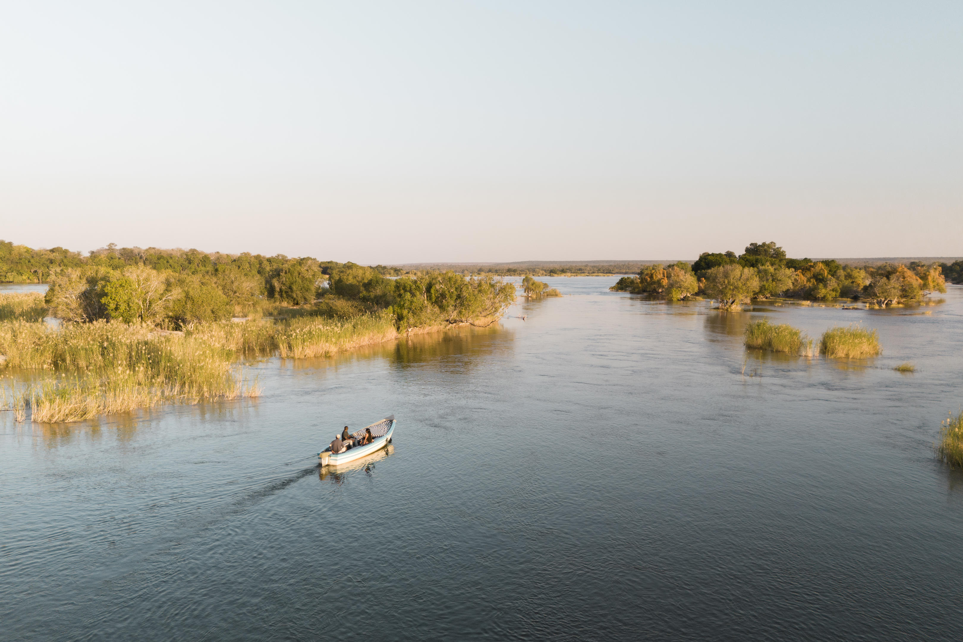 Small boat cruising through Zambezi River channels at golden hour