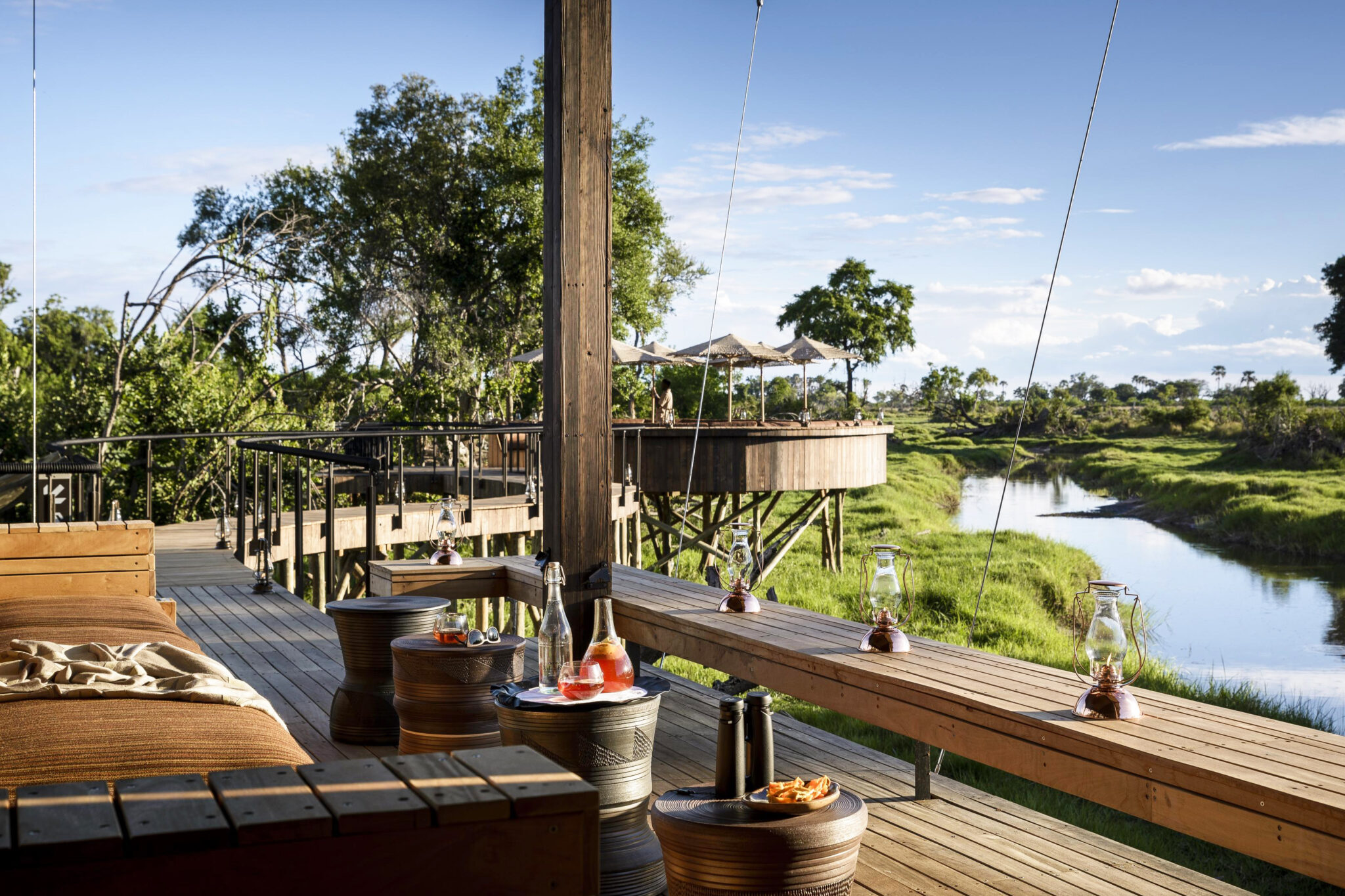 Elevated wooden deck at Xigera Camp overlooks the Okavango River, set with lanterns and cocktails.