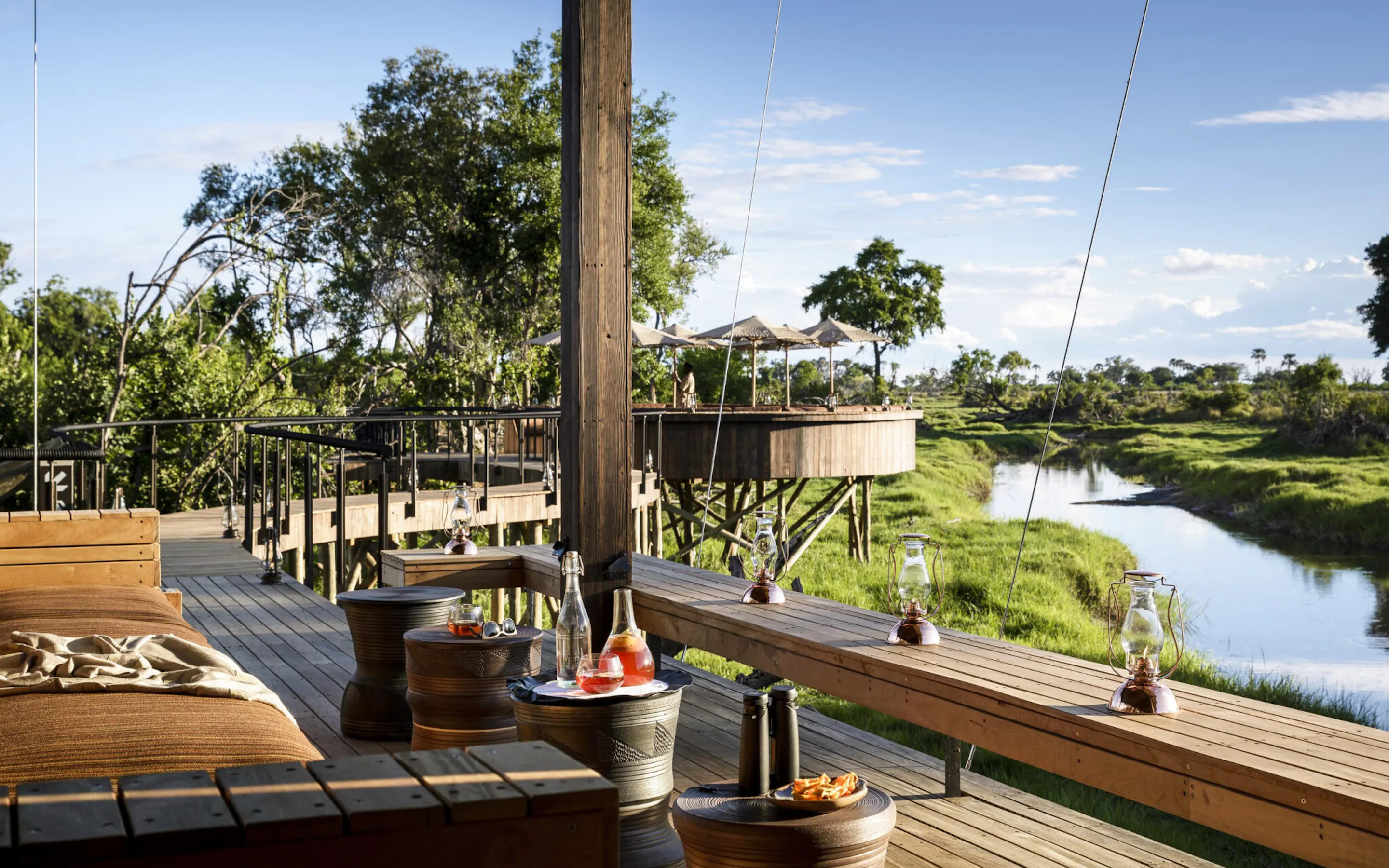 Elevated wooden deck at Xigera Camp overlooks the Okavango River, set with lanterns and cocktails.