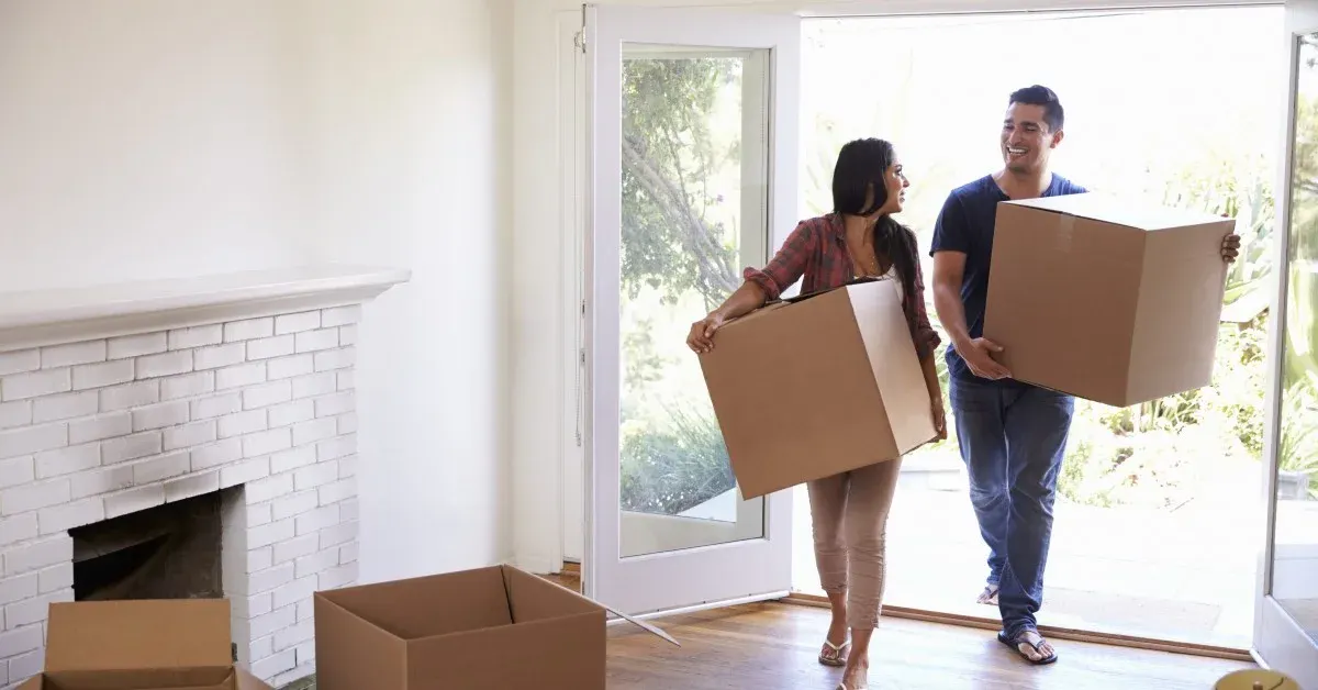 Smiling couple (female & male) moving into empty home, holding boxes