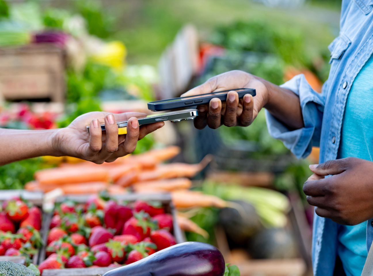 Cliente paga contactless con smartphone a un venditore in un negozio di frutta e verdura.