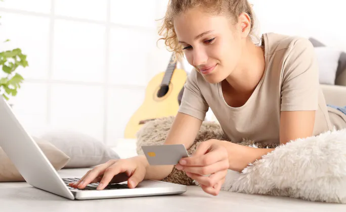 Una donna fa acquisti online da casa con un portatile e una carta di credito in mano